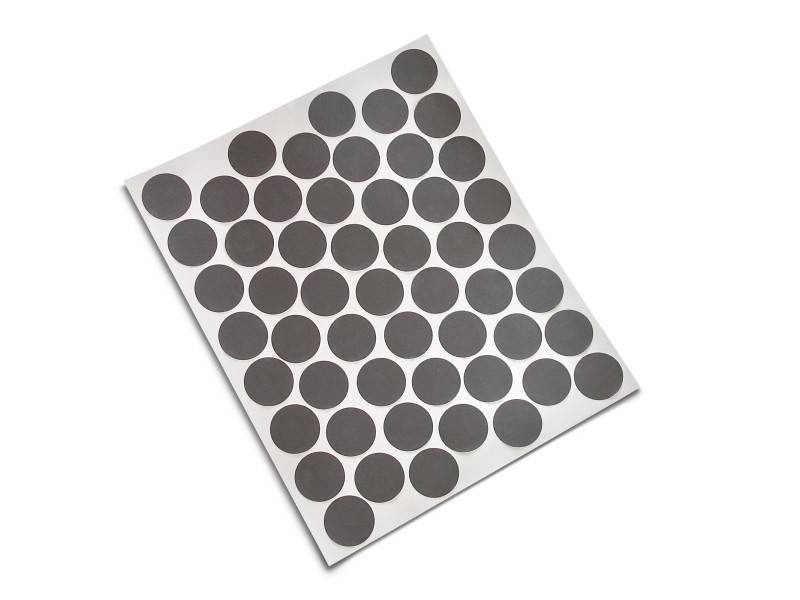 Une feuille de papier avec plusieurs rangées d'autocollants noirs, ronds, disposés de manière uniforme sur un fond blanc.