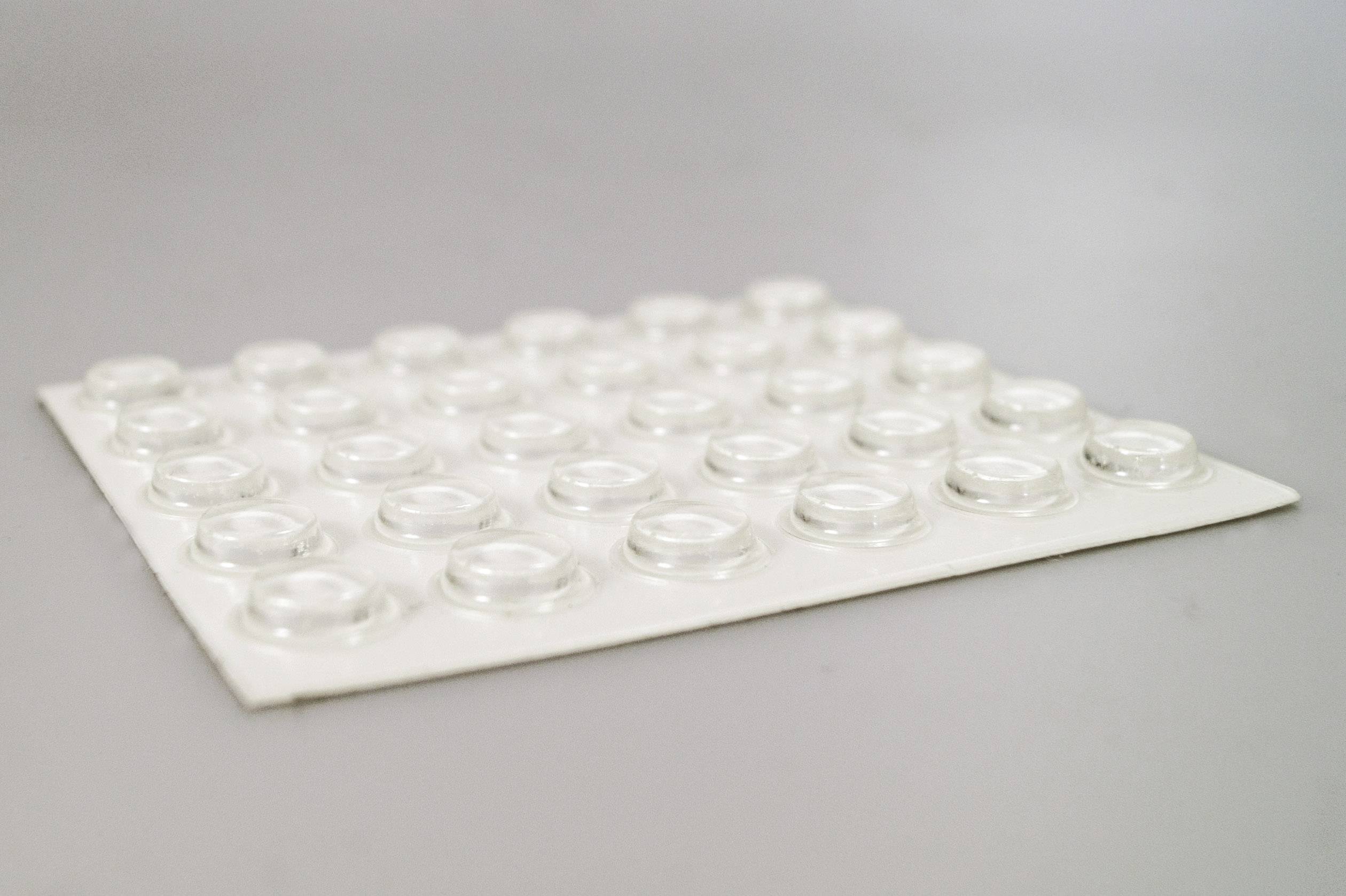 Un tapis blanc avec de nombreux petits pieds ronds en caoutchouc transparents sur une surface grise. Idéal pour rehausser et stabiliser.