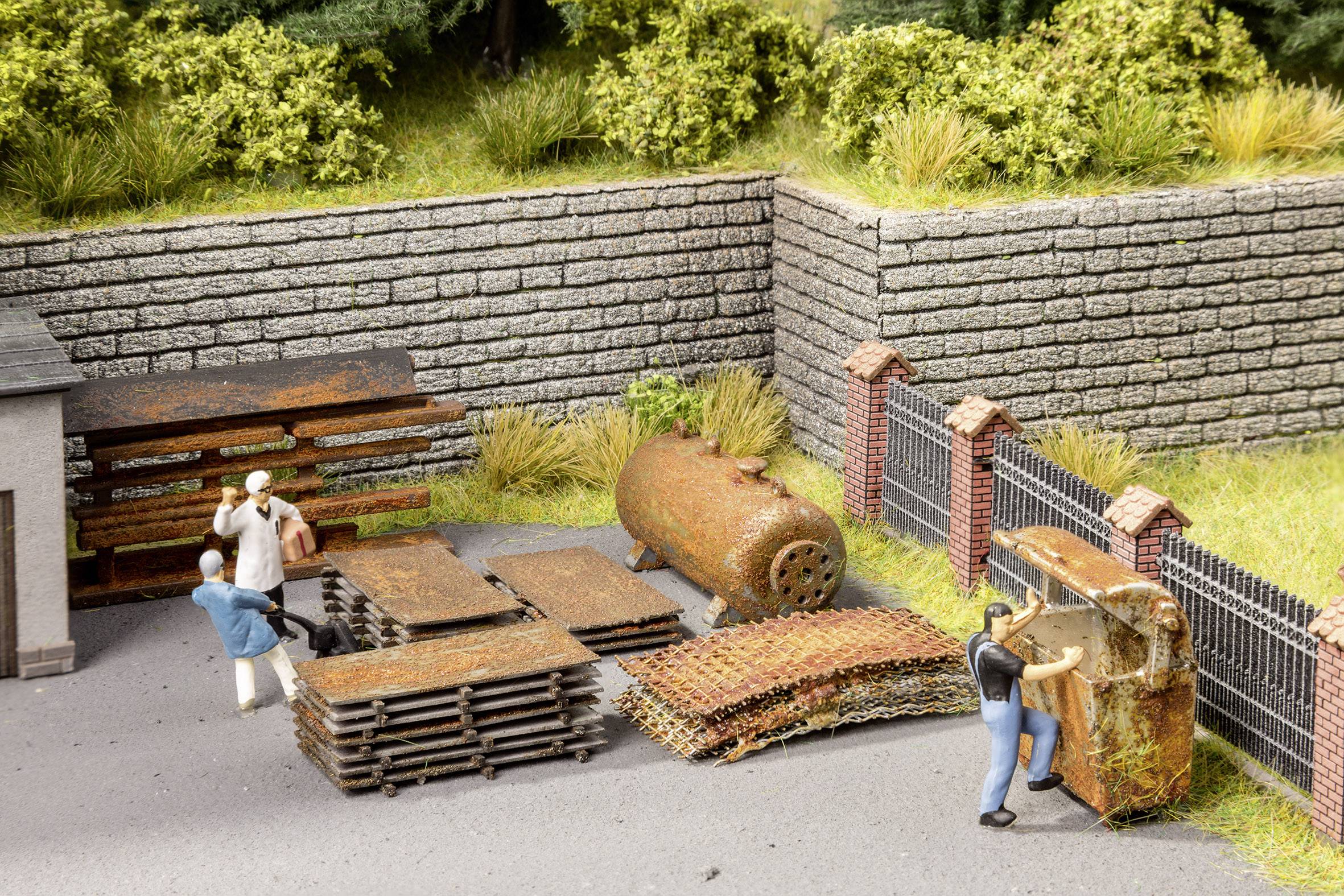Scène de modélisme ferroviaire avec des ouvriers déplaçant des plaques métalliques anciennes et rouillées ainsi qu'une chaudière dans un site industriel.