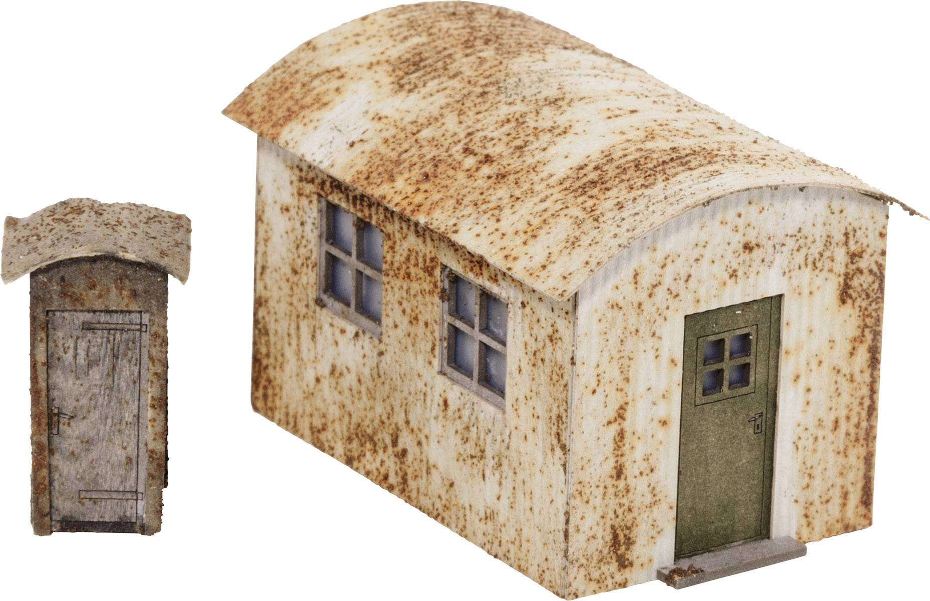 Un petit bâtiment rouillé avec deux fenêtres et une porte verte, à côté duquel se trouve un petit cabanon de toilettes assorti.