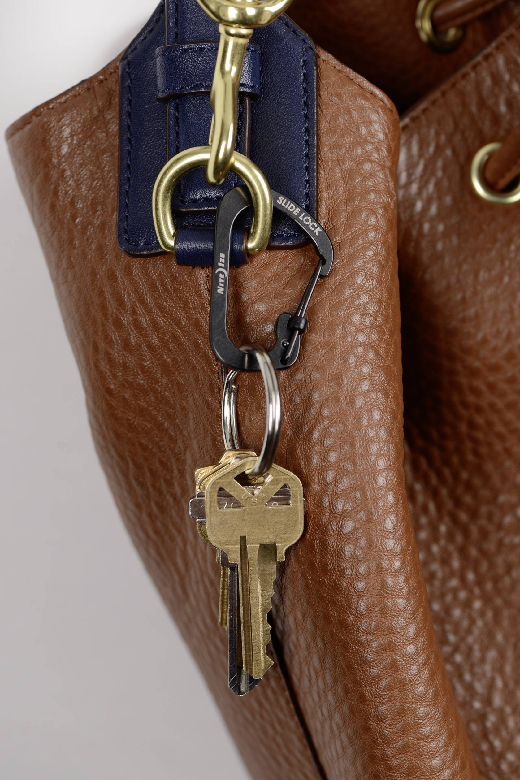 Un sac en cuir marron avec un mousqueton doré, auquel est attaché un trousseau de clés comportant plusieurs clés.
