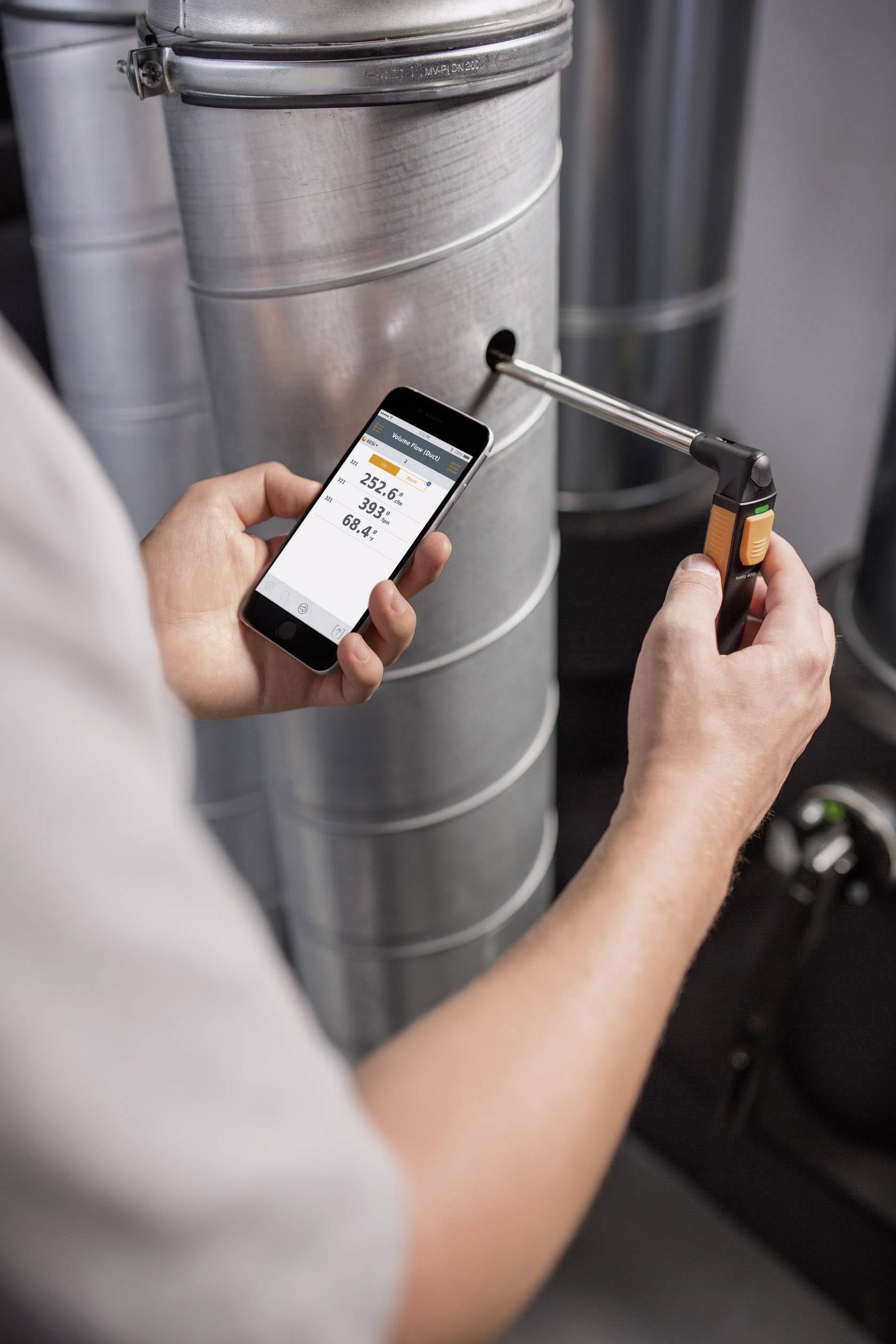 Une personne mesure la température d'un tuyau à l'aide d'un appareil. Un smartphone affiche la température, qui est lue comme étant 23,5 °C.