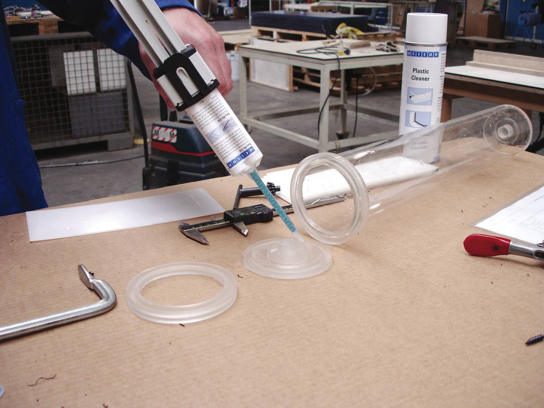 Une personne applique de la colle sur un anneau en plastique pour assembler un tube transparent. Des outils sont visibles en arrière-plan.