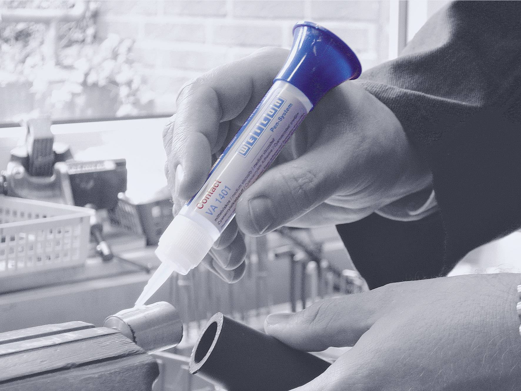 Une personne applique de la colle à partir d'un tube sur un tuyau dans un atelier, probablement pour une réparation ou un montage.