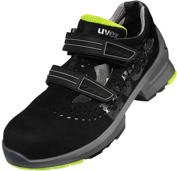 Une chaussure de sécurité noire avec deux fermetures velcro et une semelle verte. Le matériau supérieur présente des détails perforés pour une meilleure respirabilité.