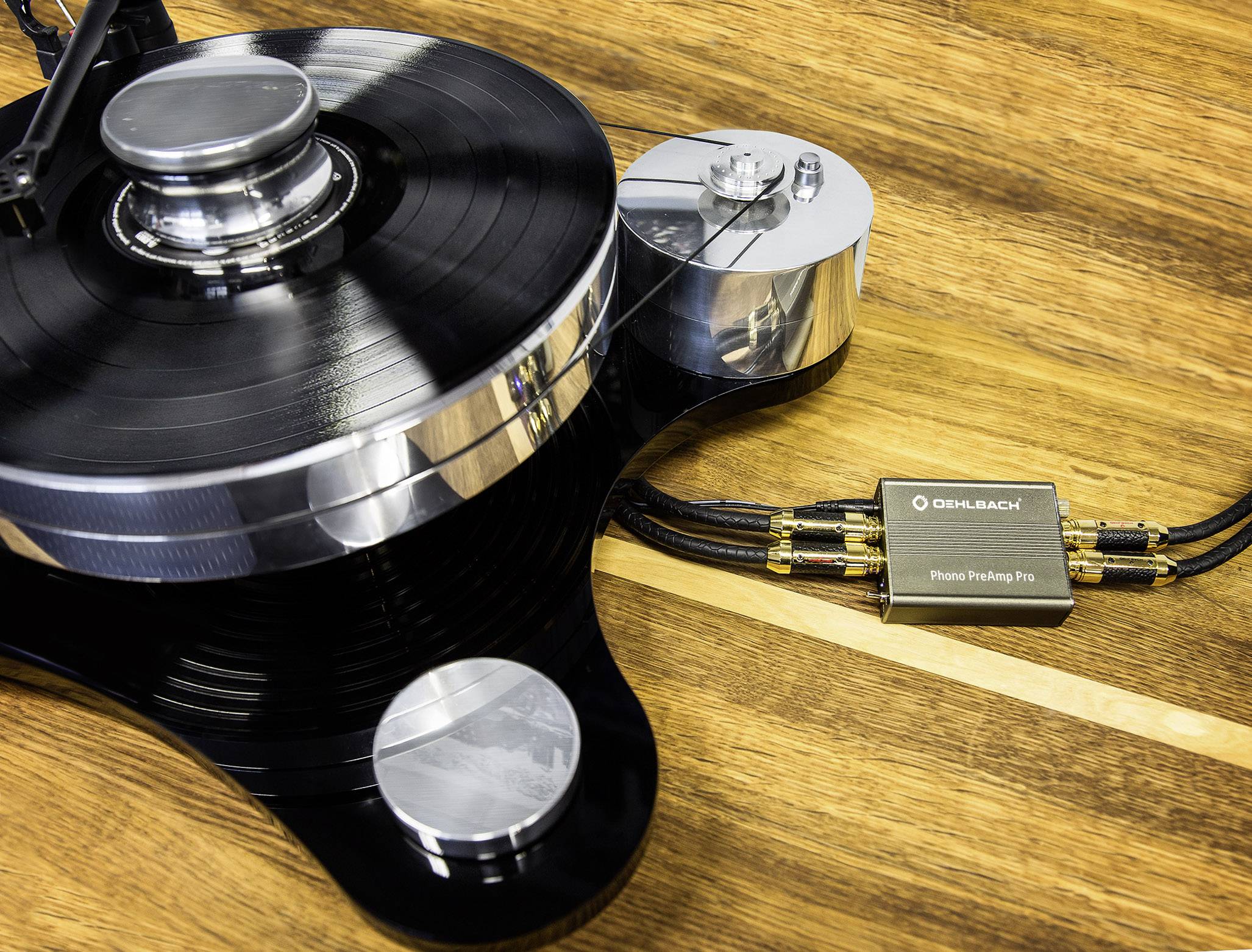 Tourne-disque avec un disque vinyle noir et un câble phono sur une table en bois ; surfaces métalliques et mates.