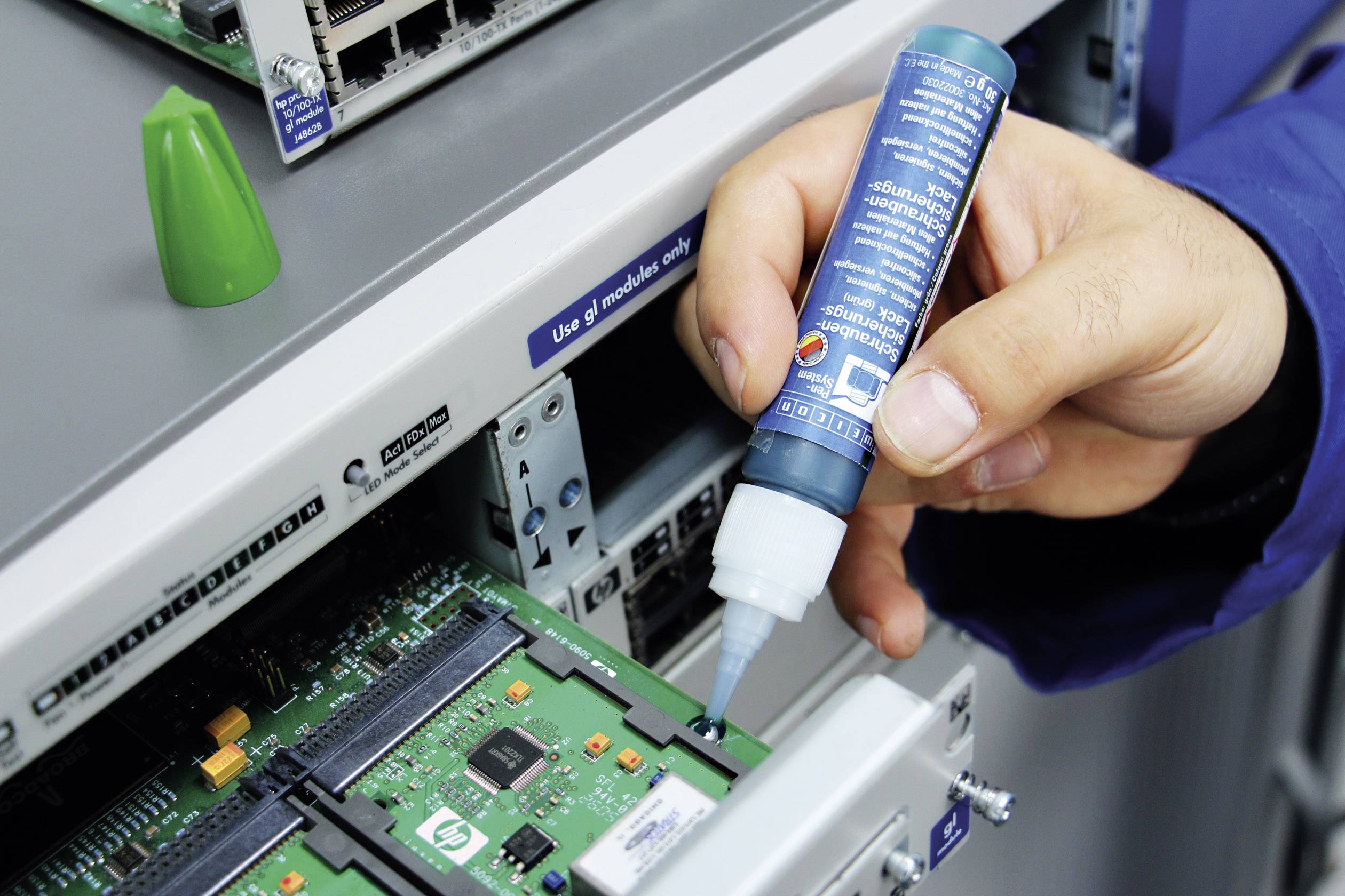 Une personne applique une substance à partir d'un petit flacon bleu sur une carte de circuit imprimé dans une salle de serveurs.