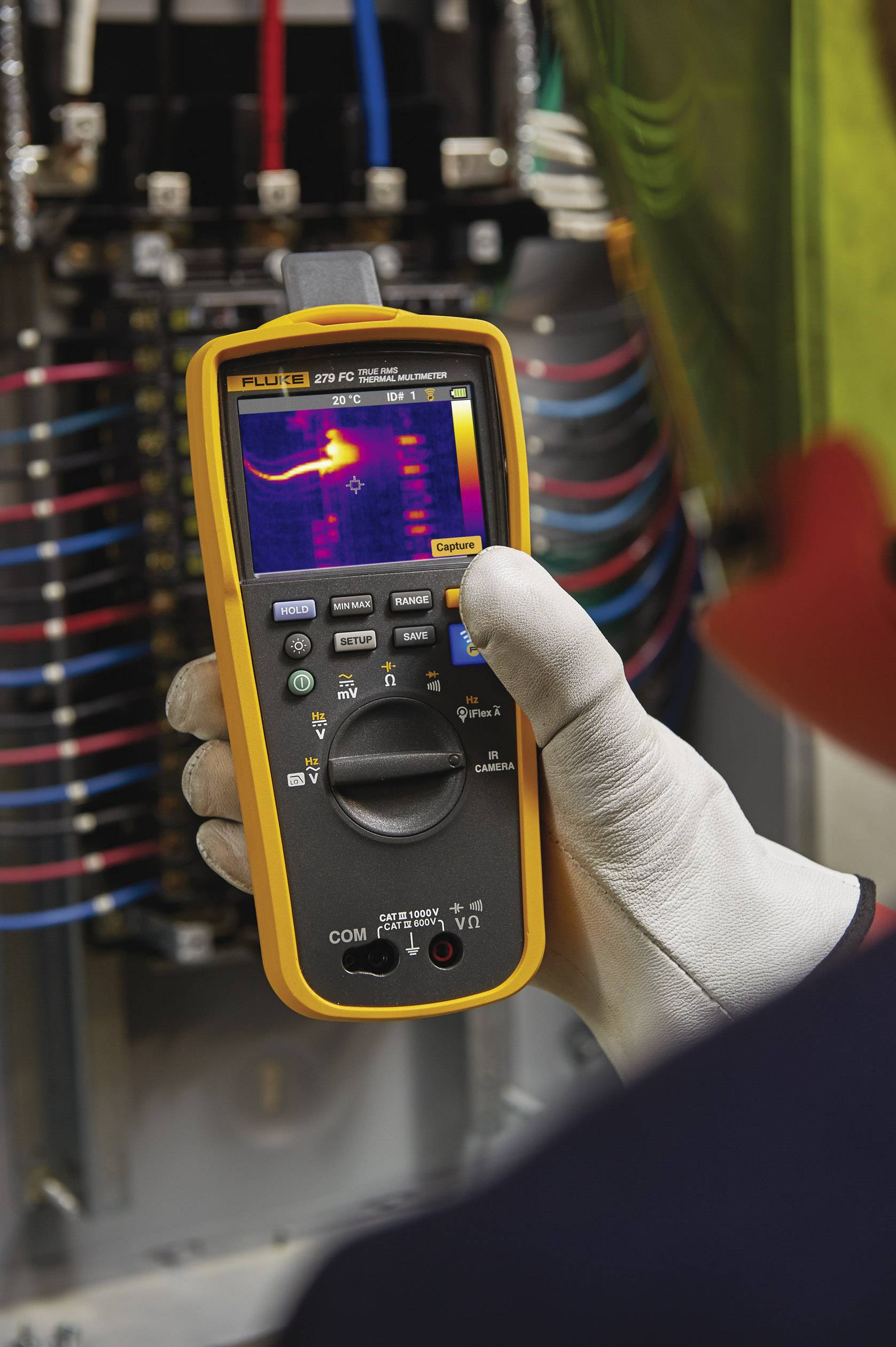 Une personne utilise un multimètre numérique avec fonction thermographique pour vérifier les composants électriques dans un armoire électrique.