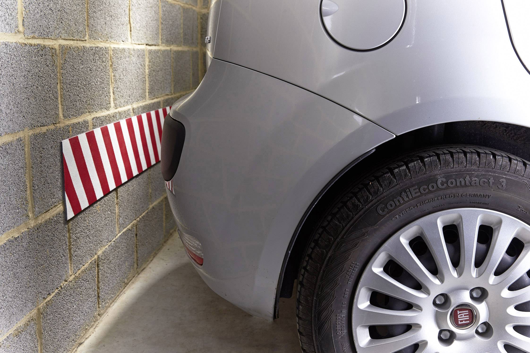 Une voiture dans un garage, près d'un mur à rayures rouges et blanches indiquant la distance. La voiture est une Fiat équipée de pneus ContiEcoContact.
