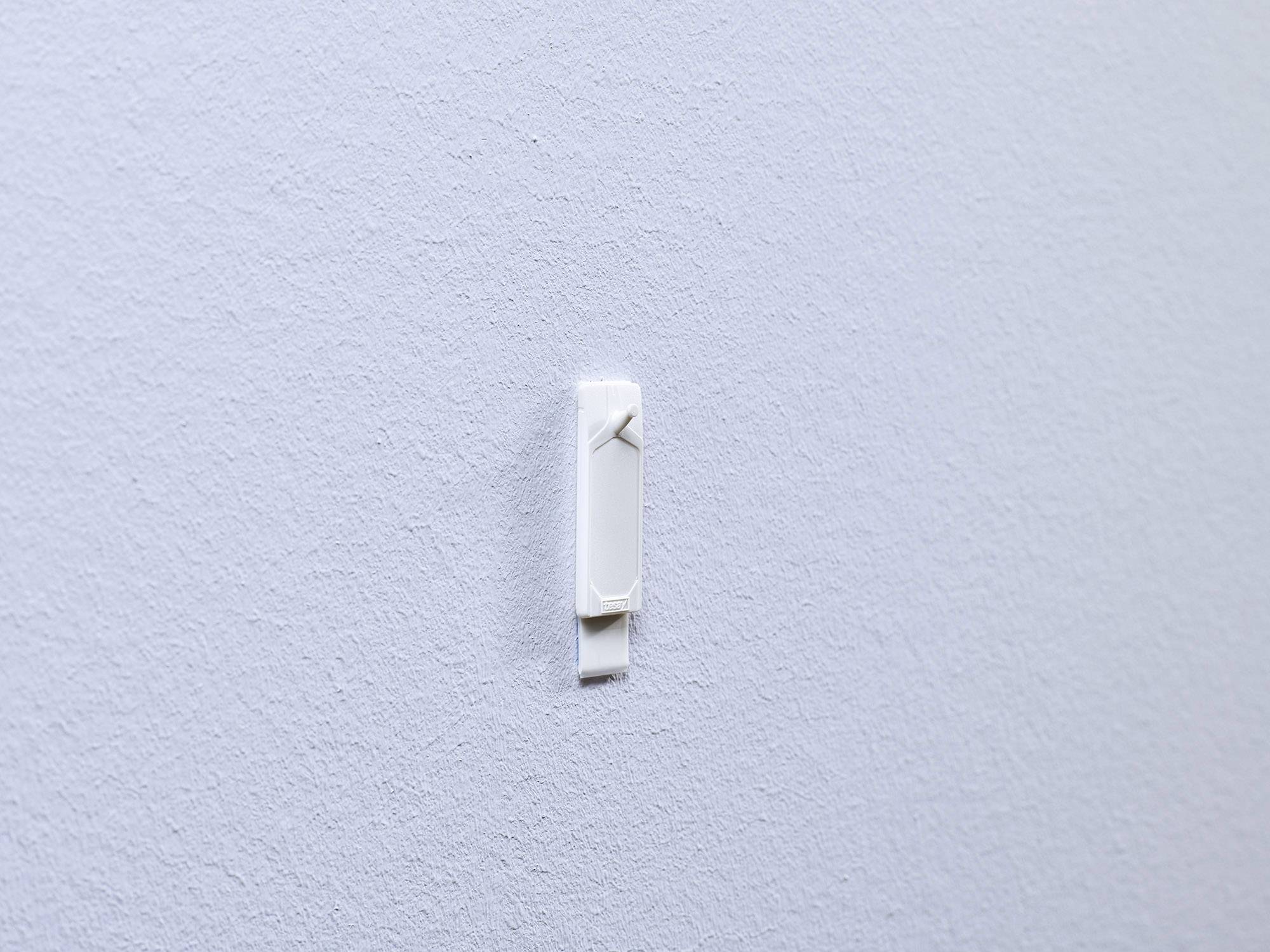 Un crochet blanc sur un mur lisse et gris. Le crochet est vide et fixé de manière centrale sur le mur.