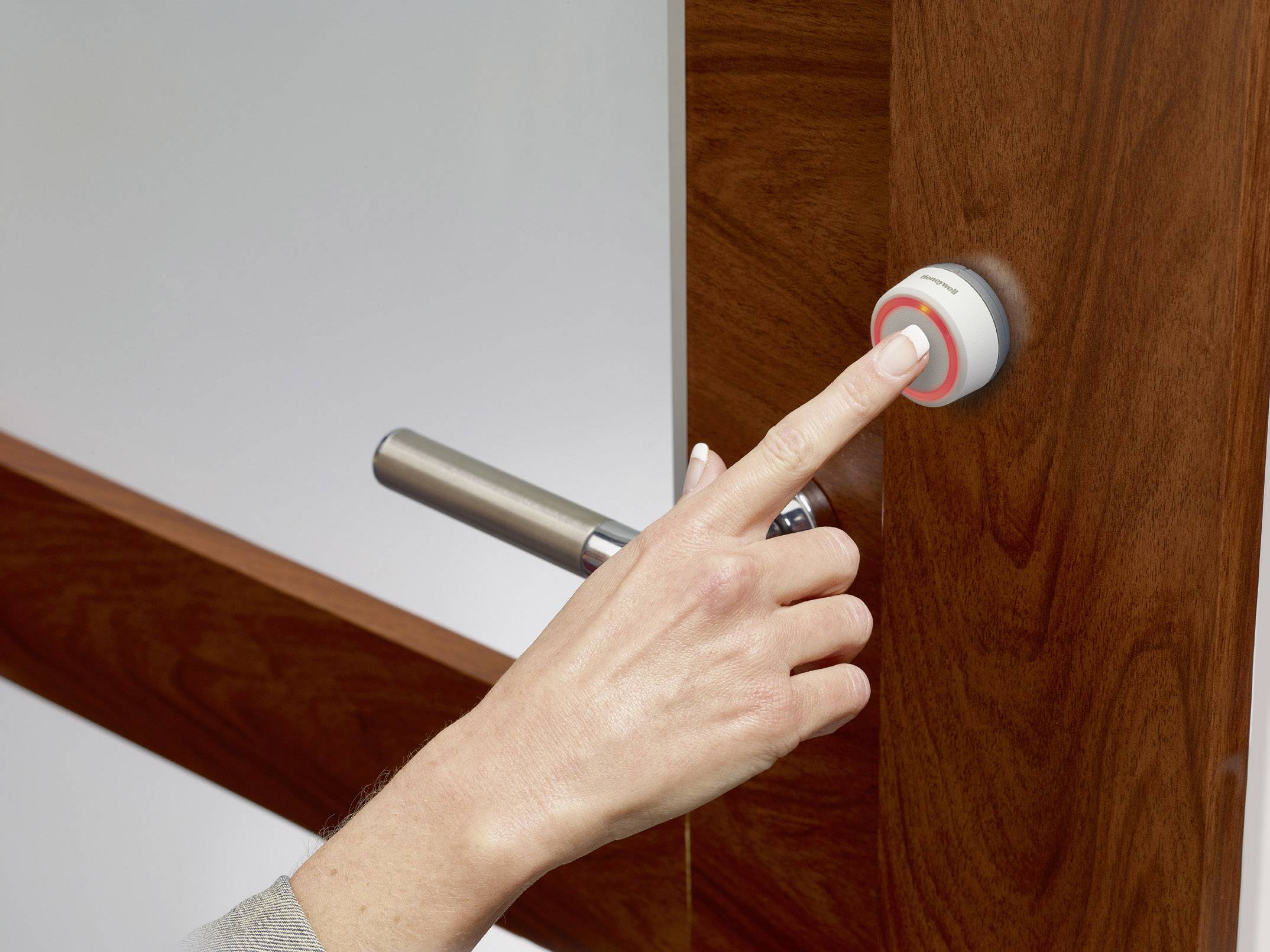 Une main appuie sur un bouton d'ouverture de porte rond à côté d'une porte en bois avec une poignée argentée.