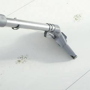 Un embout d'aspirateur gris nettoie une surface carrelée blanche avec des taches de saleté visibles.