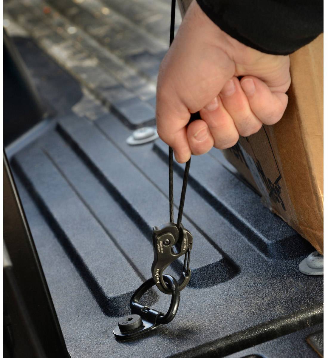 Une personne tient un cordon élastique avec un crochet, fixé à une surface noire, probablement pour sécuriser un objet.
