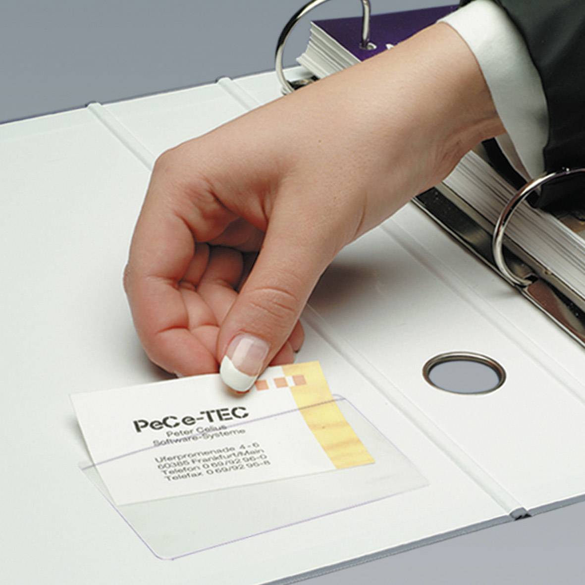 Une main glisse une carte de visite portant l'inscription 'PeCe-TEC Paper' dans un classeur blanc. Le classeur est posé sur une table.