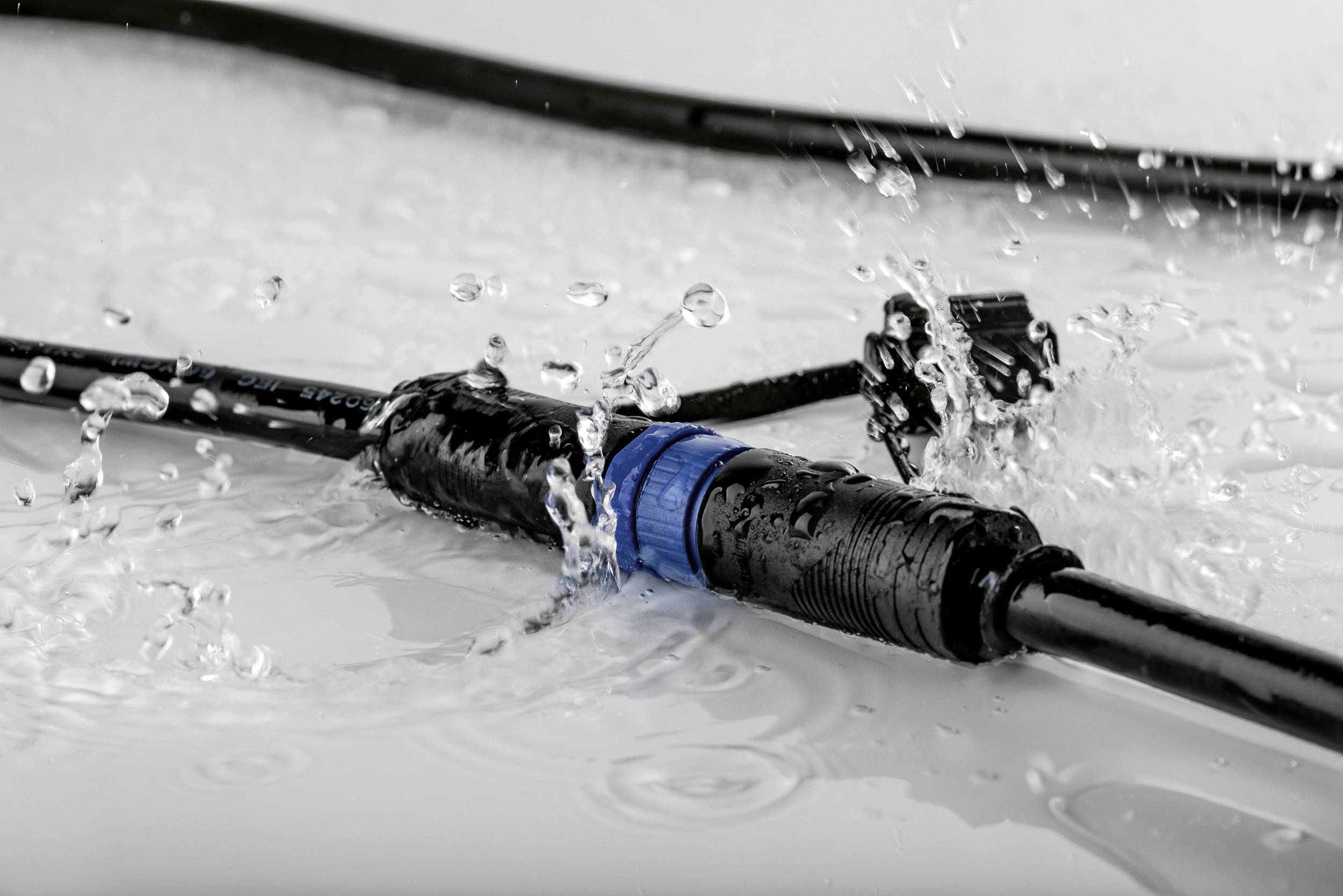 Un connecteur de câble étanche en gros plan, protégé contre les éclaboussures et entouré de gouttes d'eau, illustre sa robustesse.