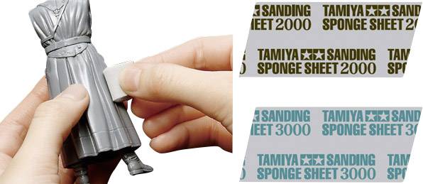 Une main ponce une figurine grise avec une éponge abrasive TAMIYA. À droite sont représentés des éponges abrasives TAMIYA aux grains 2000 et 3000.
