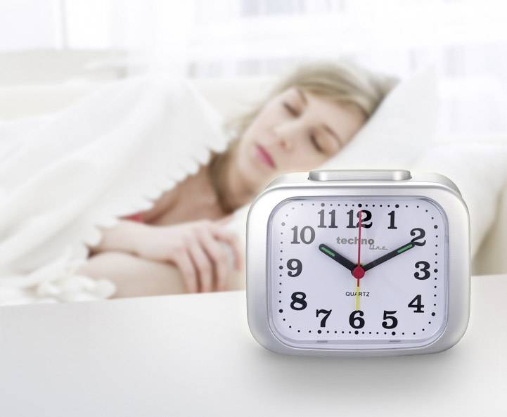 Une femme dort sous une couverture en arrière-plan. Au premier plan, un réveil affiche 7h10.