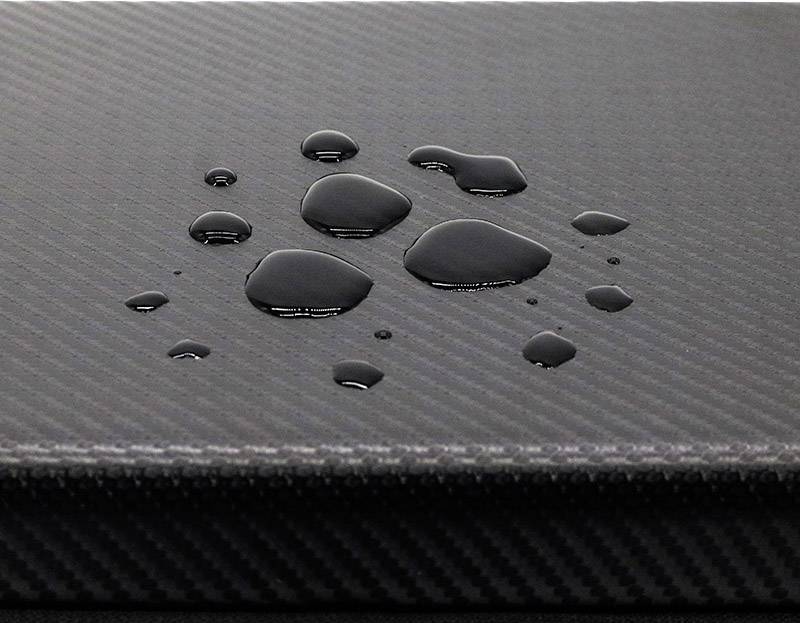 Gouttelettes d'eau sur une surface sombre structurée, probablement hydrofuge.