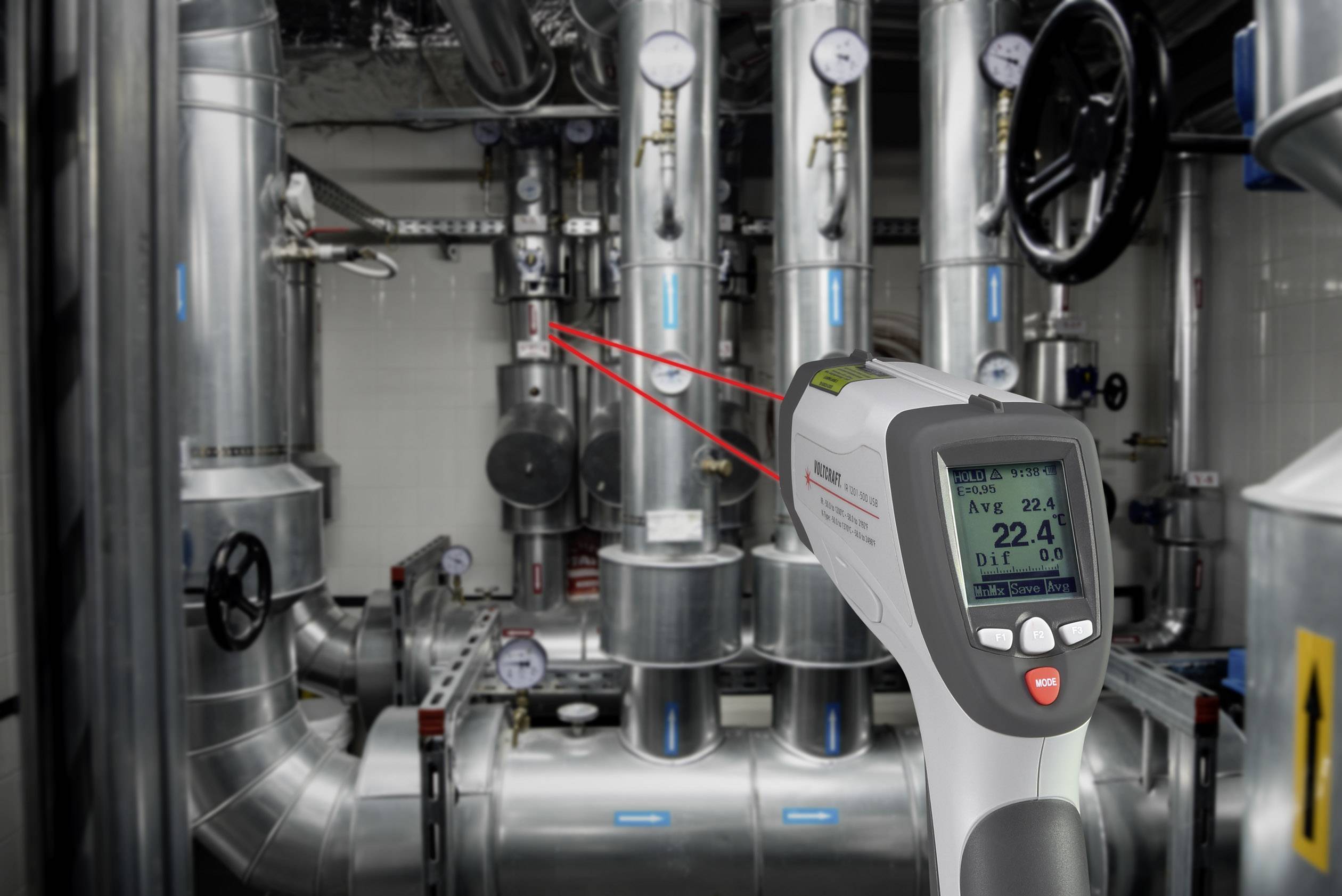Un thermomètre infrarouge numérique mesure la température des tuyaux dans une installation industrielle. L'affichage indique '22,4 °C'.