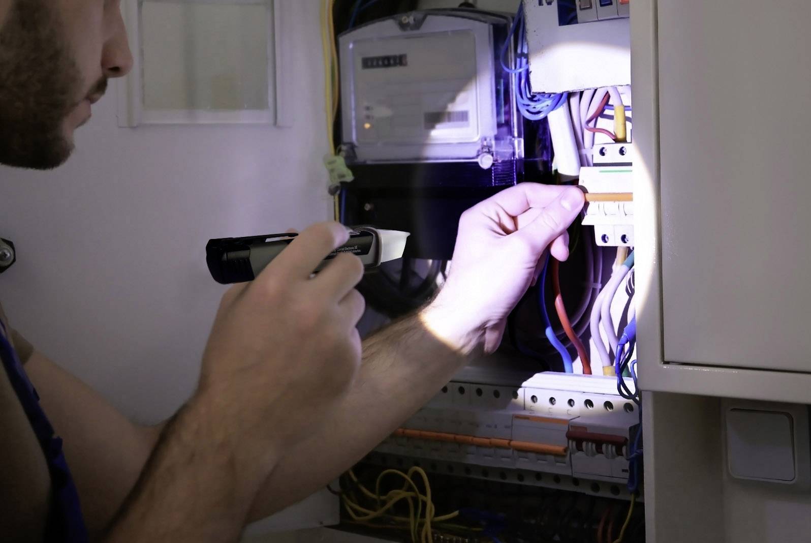 Une personne travaille avec une lampe de poche sur un boîtier électrique ouvert et vérifie les connexions de câbles.
