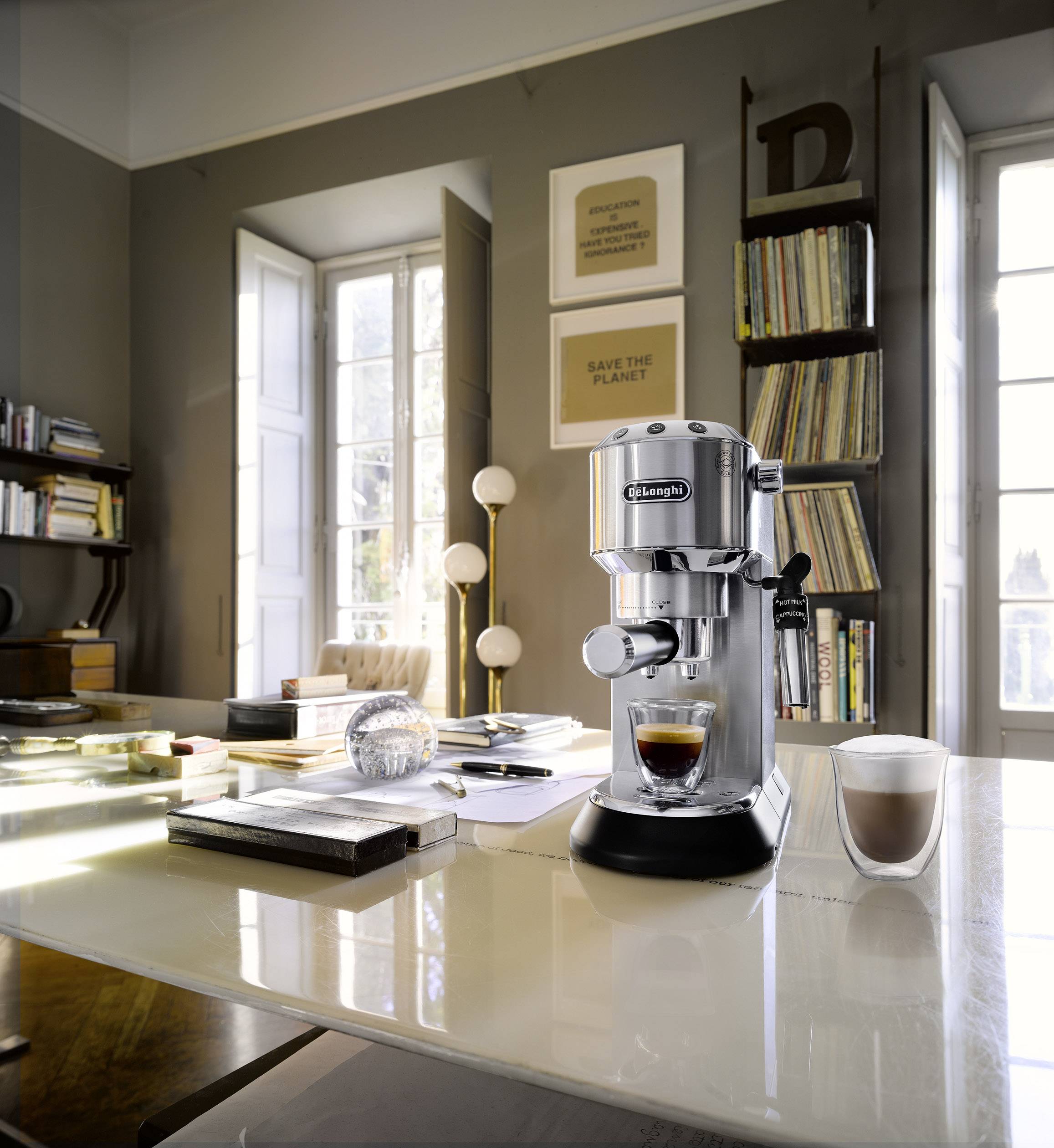 Machine à café posée sur une table dans une pièce bien éclairée, avec un espresso et un cappuccino. Des étagères et une fenêtre sont visibles en arrière-plan.