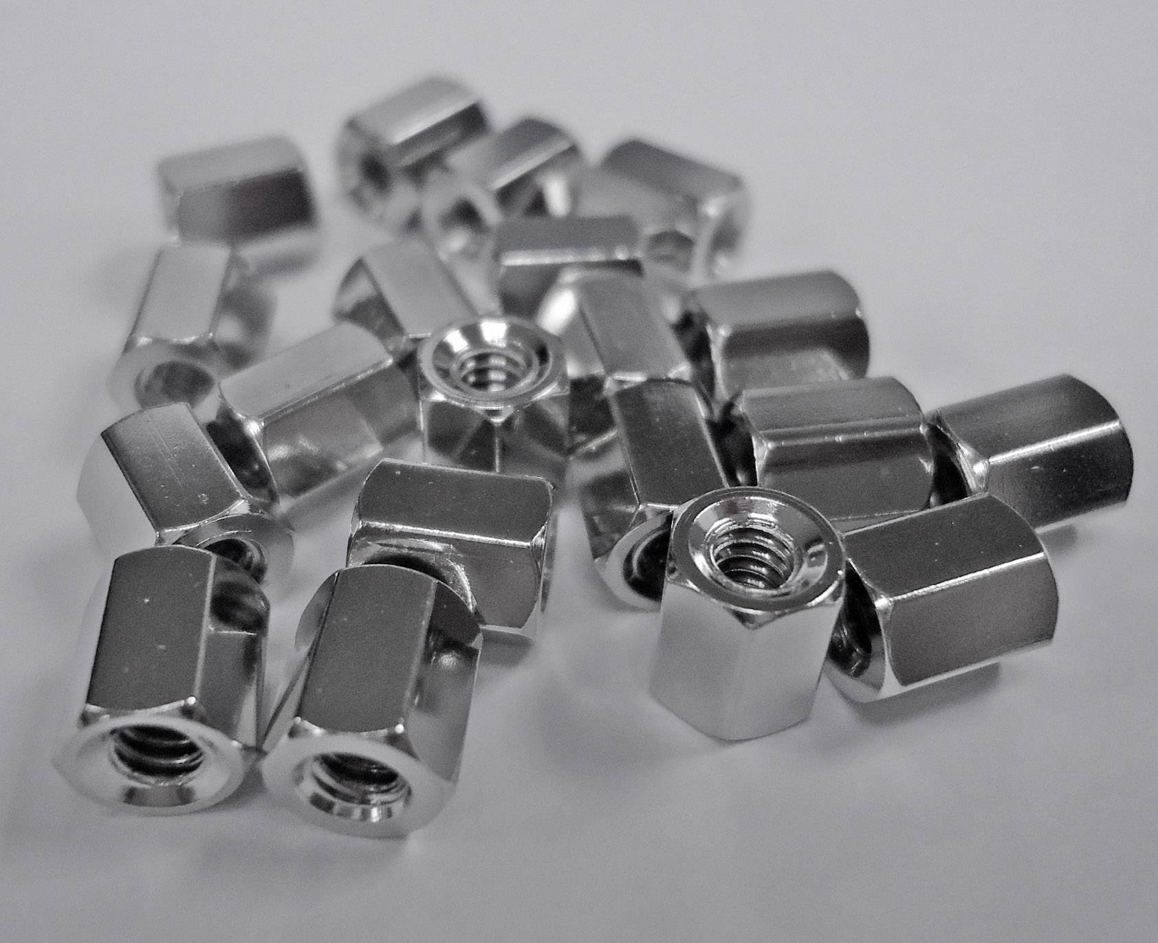 Plusieurs écrous hexagonaux argentés sont répartis de manière irrégulière sur une surface blanche.