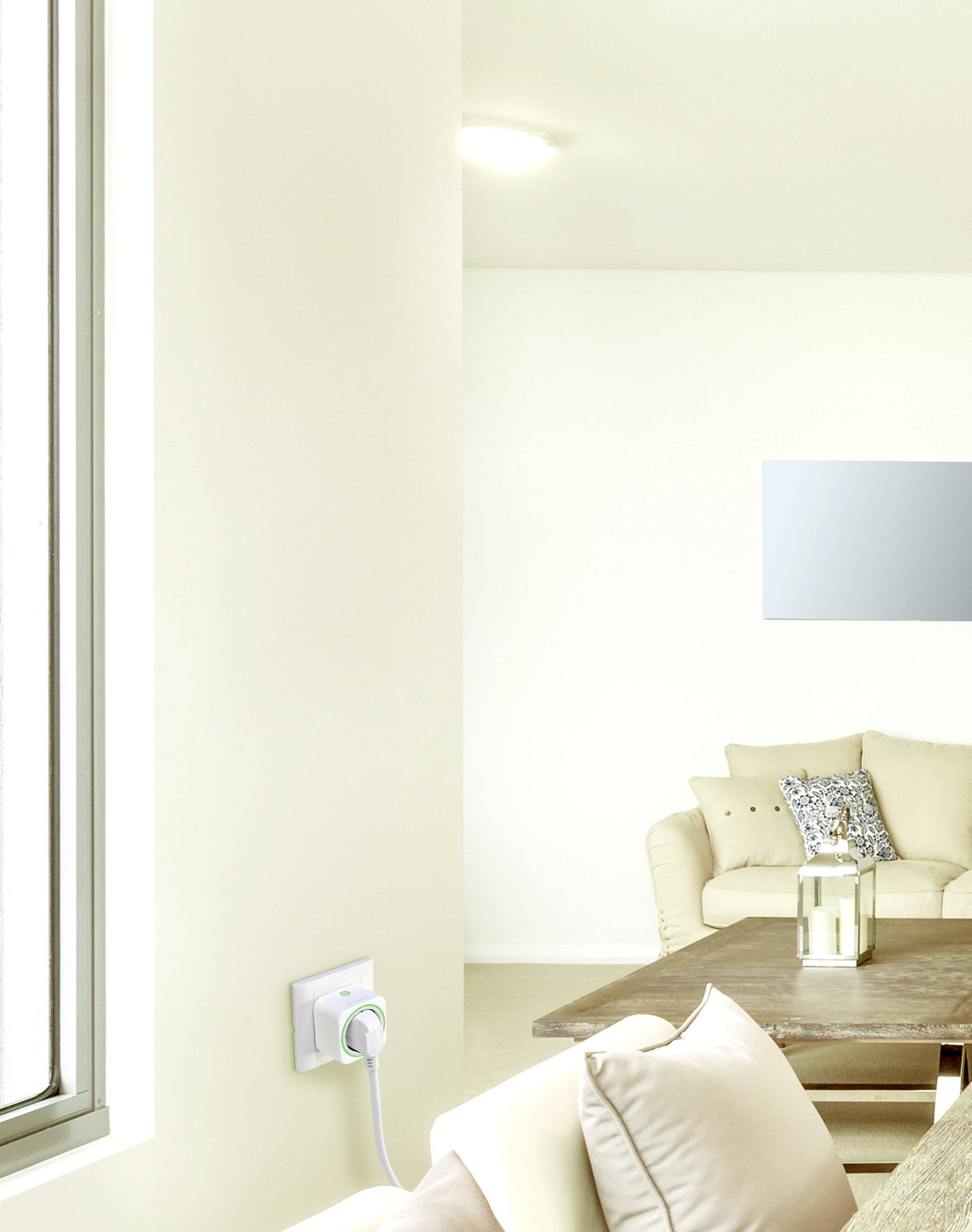 Salon lumineux avec un canapé beige et une table en bois. Une fenêtre à gauche et une lumière ronde au plafond. Un appareil accroché au mur.