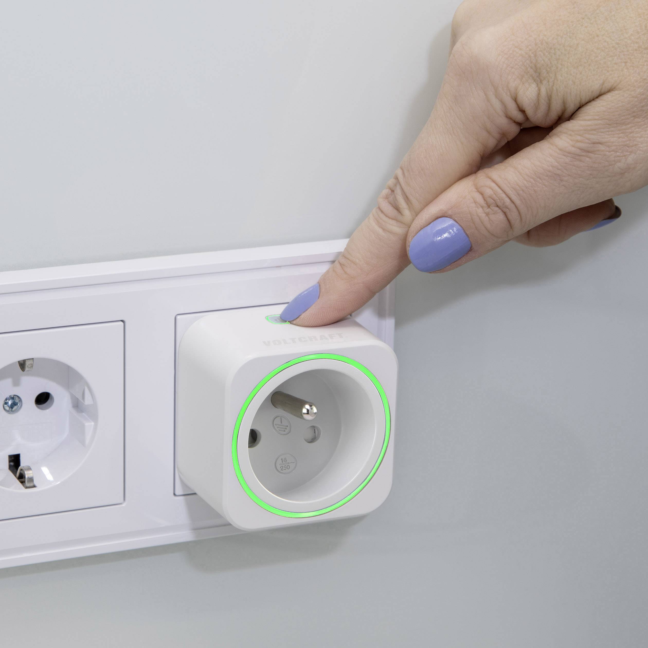Une main appuie sur une prise intelligente branchée dans une prise murale. Un anneau lumineux vert indique que l'appareil est sous tension.