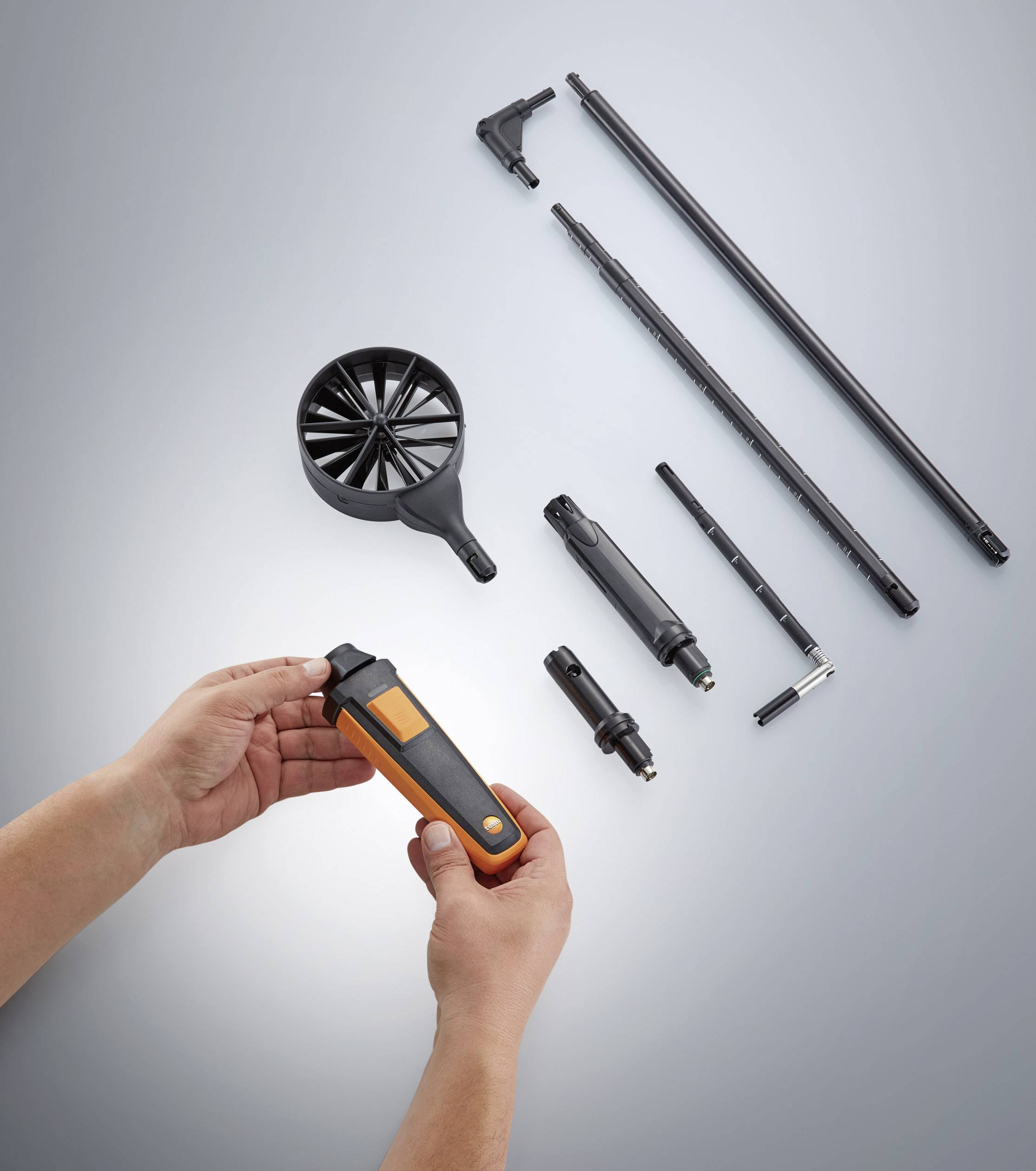 Quelques instruments de mesure et pièces accessoires sont disposés sur une table. Deux mains tiennent un appareil orange de la taille d'une main, prêt à être utilisé.