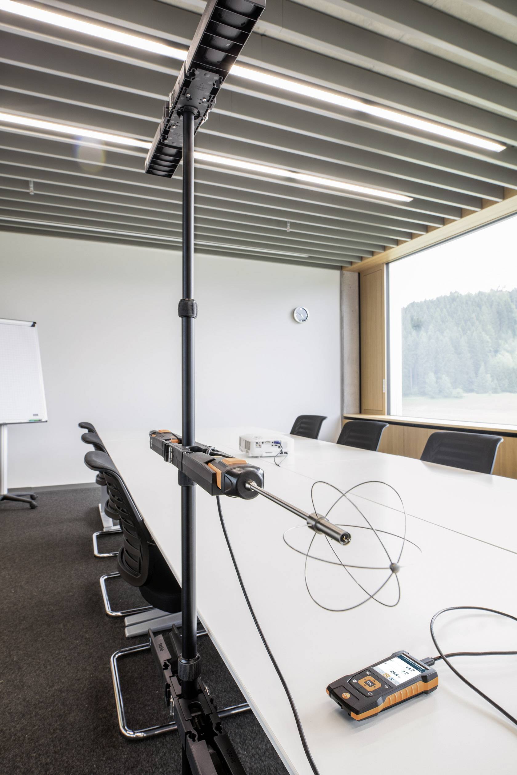 Une salle de réunion avec une longue table, des chaises et une vue sur la fenêtre. Sur la table se trouve un appareil de mesure avec antenne pour l'acoustique de la pièce.