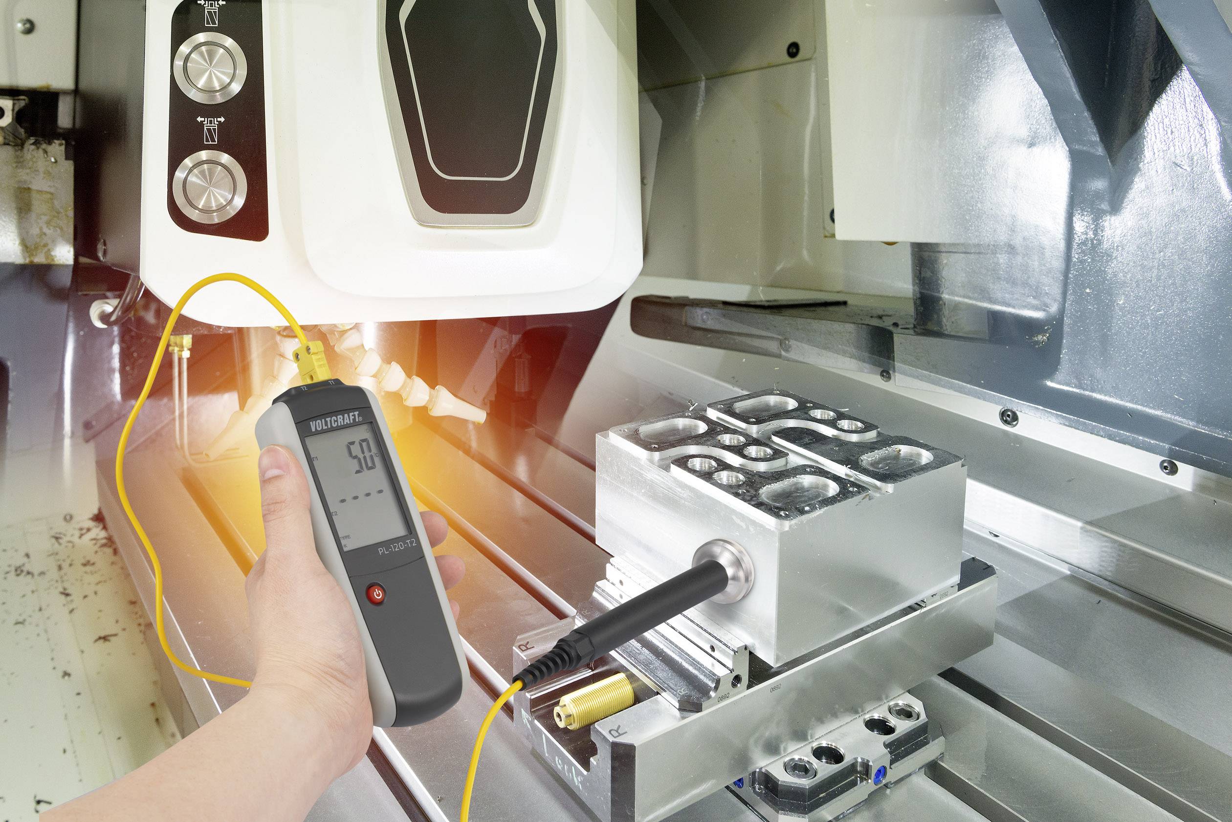 Une personne mesure la température d'un bloc métallique à l'aide d'un thermomètre numérique dans un environnement d'atelier.