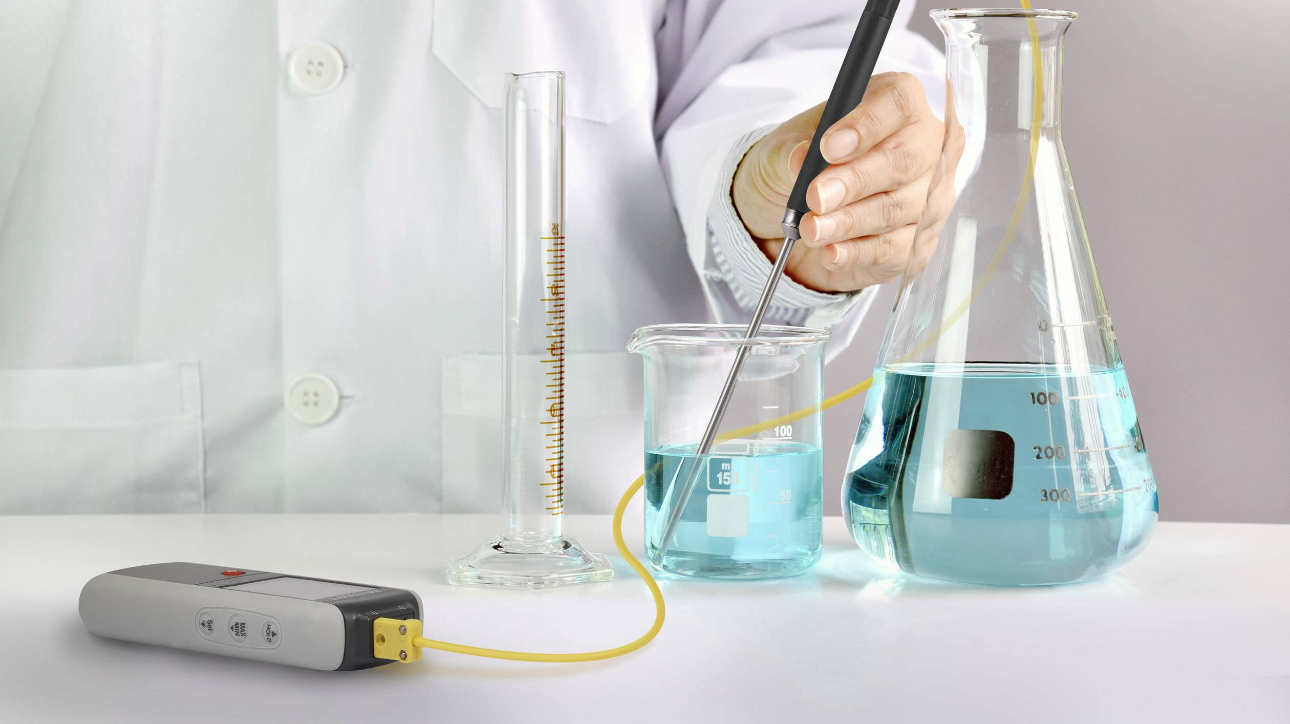Une personne en blouse de laboratoire mesure le pH d'un liquide bleu dans un bécher à l'aide d'un appareil de mesure.