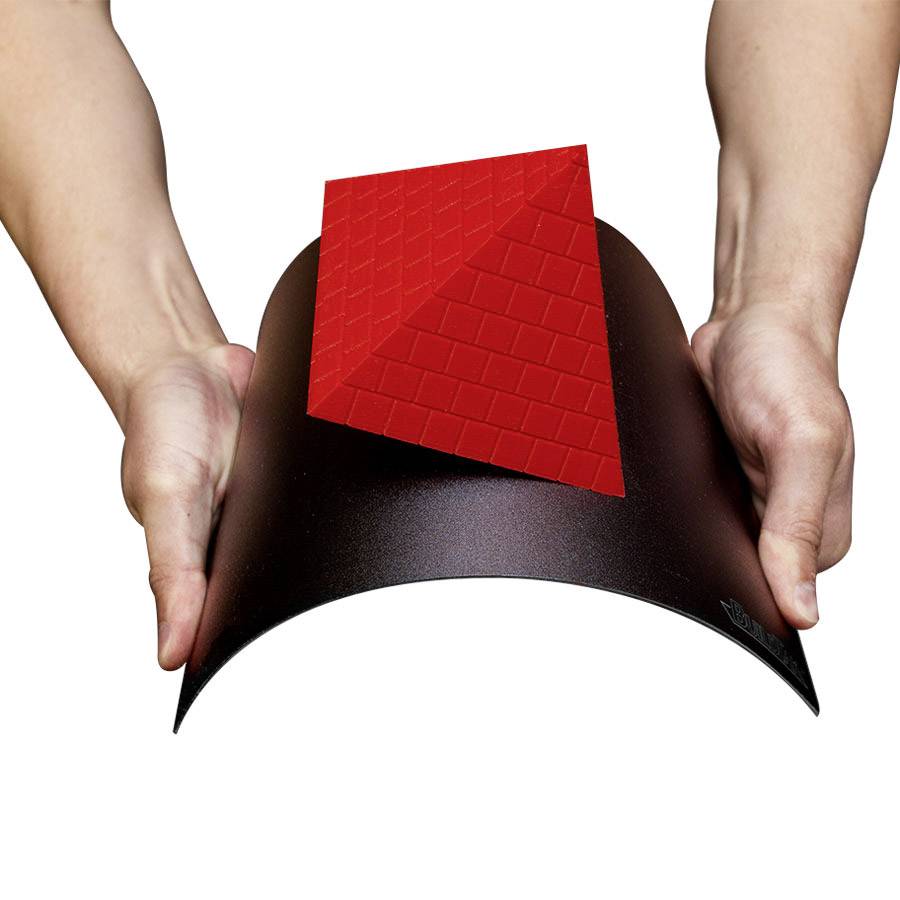 Deux mains tiennent un tissu noir ou un tapis portant une construction 3D rouge en forme de pyramide.