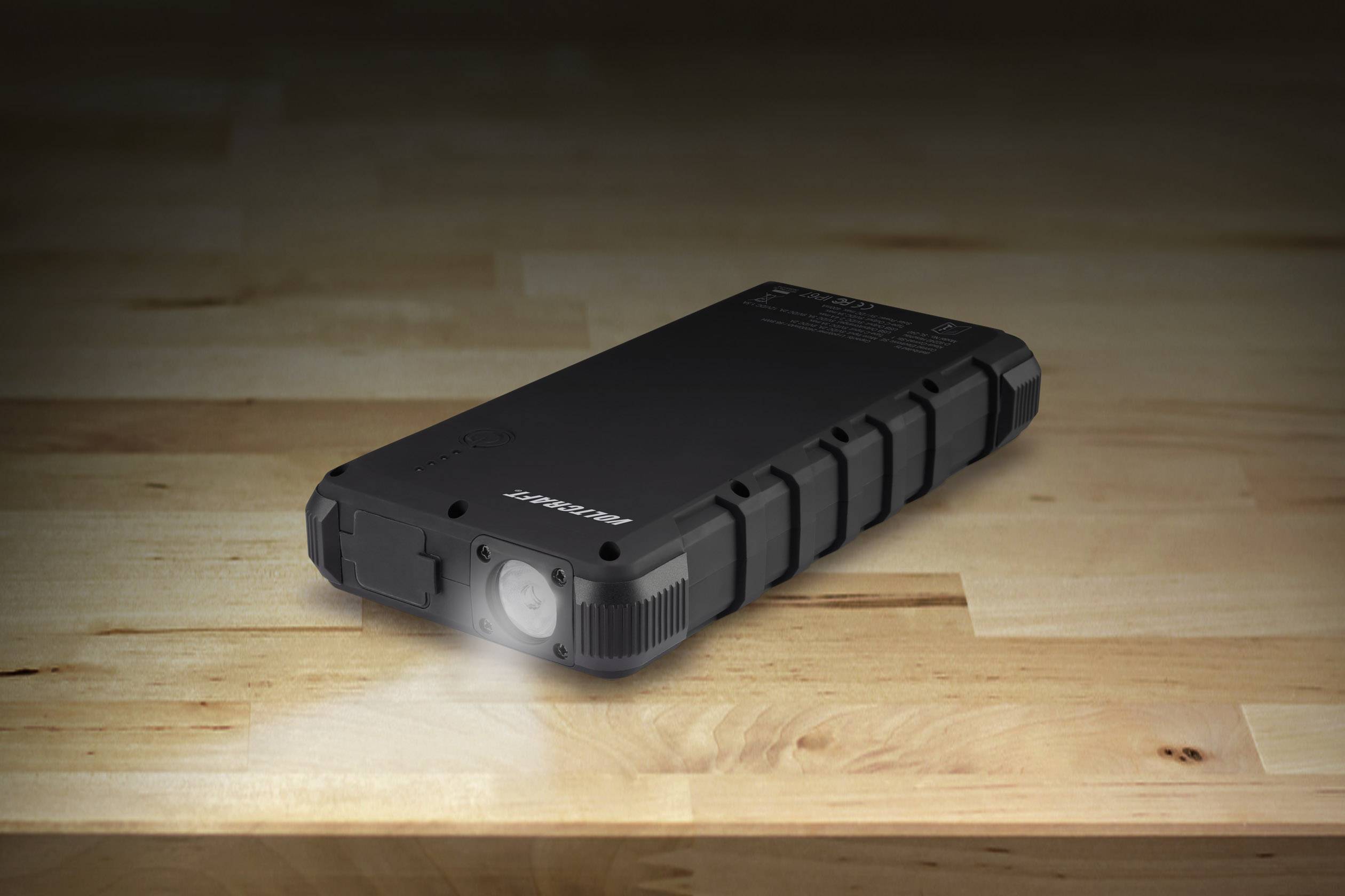 Batterie externe noire et compacte, au design robuste avec fonction lampe torche, posée sur une table en bois.