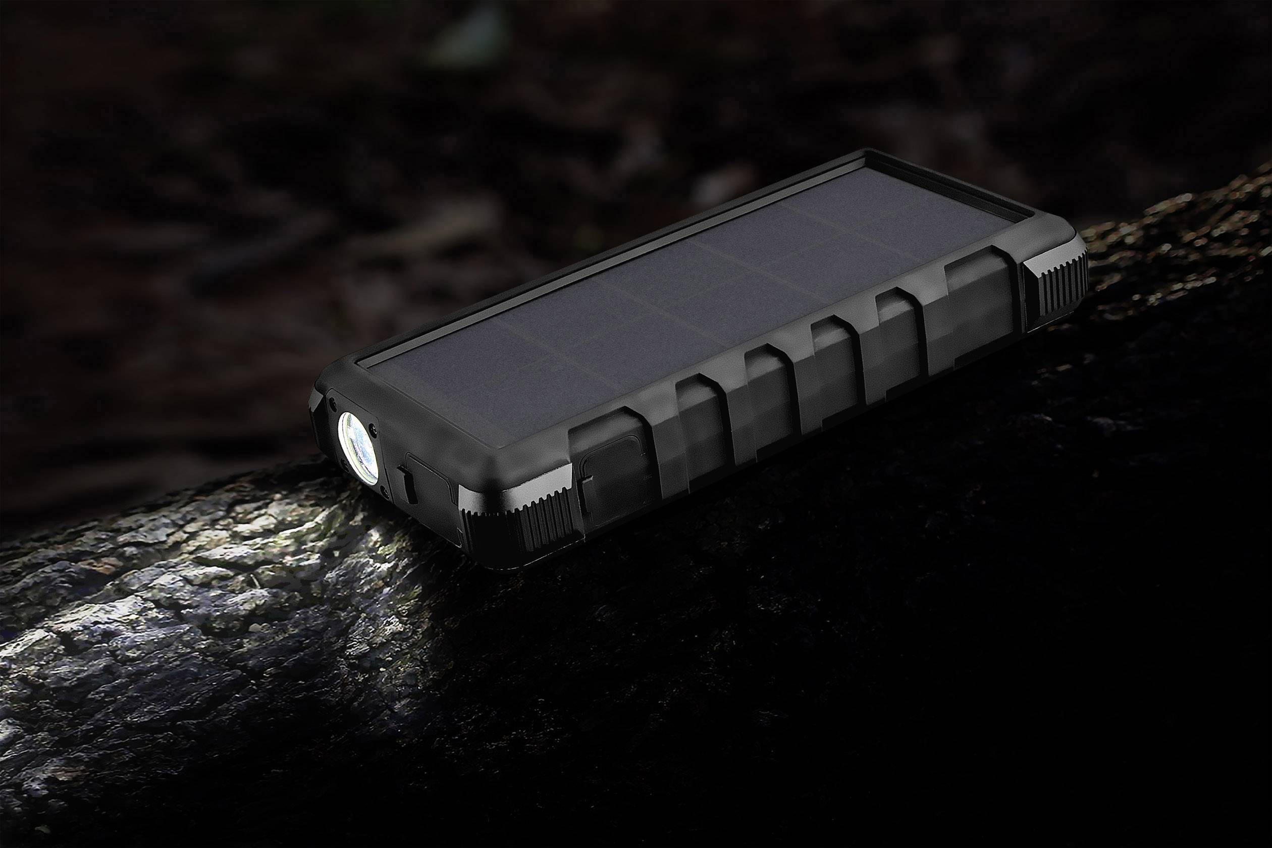 Une batterie externe solaire noire avec lampe de poche intégrée est posée sur un tronc d'arbre dans l'obscurité.