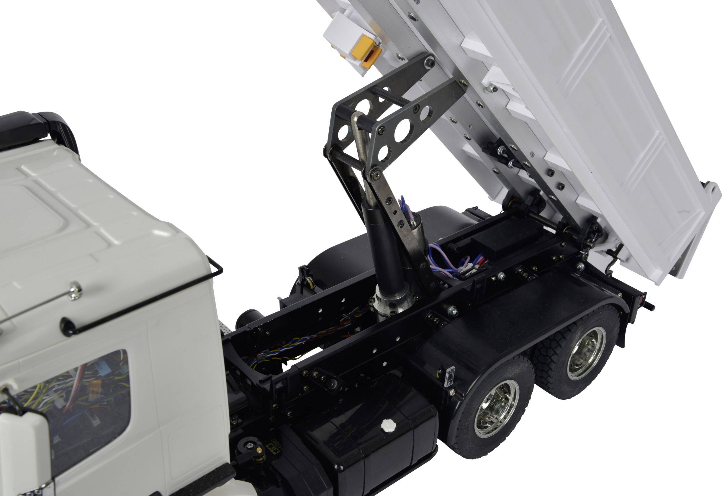 Un camion blanc avec un mécanisme basculant soulève la surface de chargement. L'accent est mis sur le système hydraulique à l'arrière du véhicule.