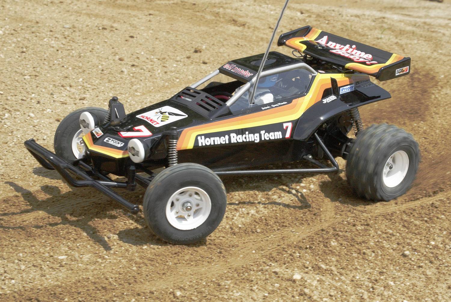 Une voiture télécommandée portant l'inscription 'Hornet Racing Team', roule sur une piste poussiéreuse.