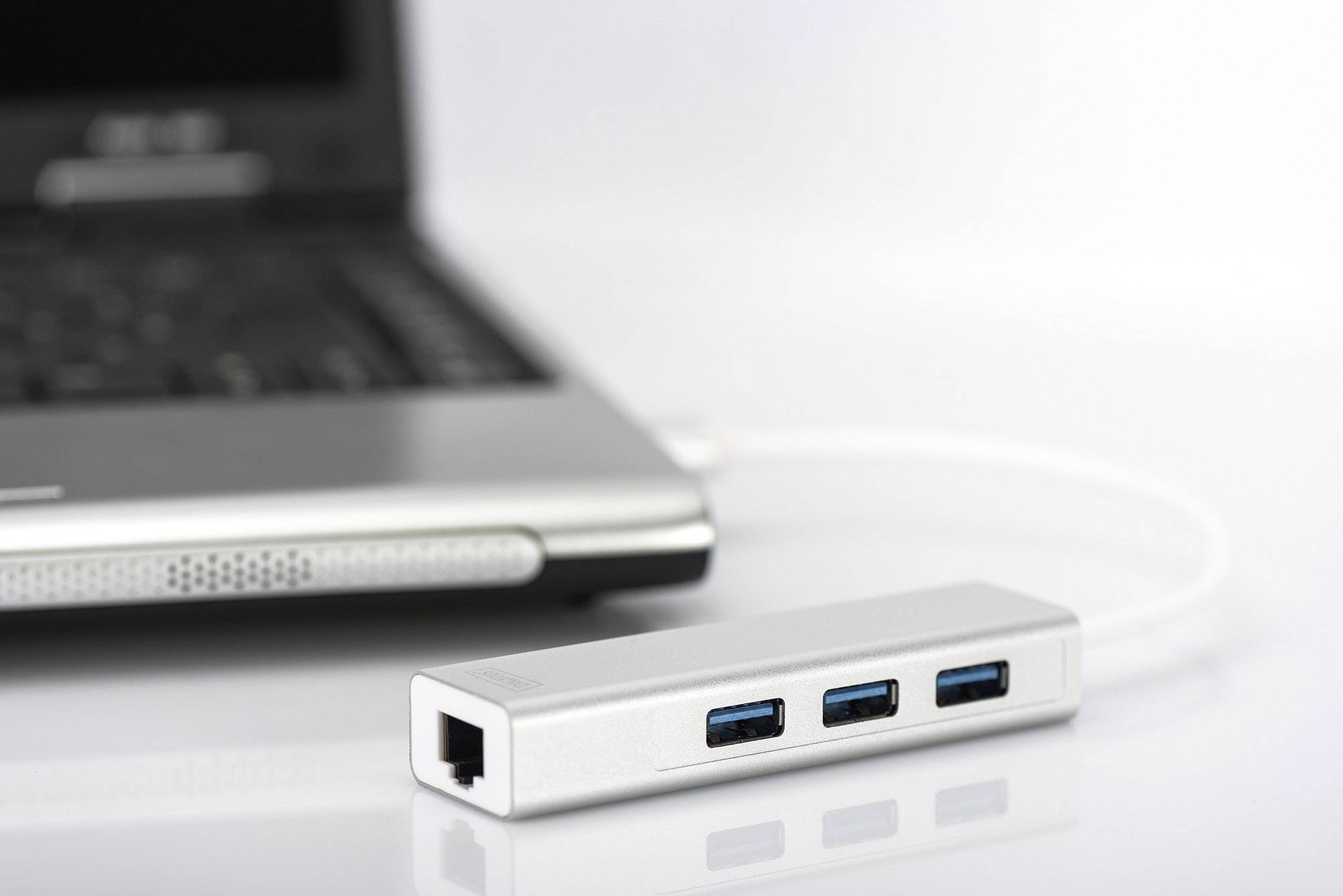 Hub USB argenté avec trois ports USB 3.0 bleus, connecté à un ordinateur portable ouvert sur un fond blanc.