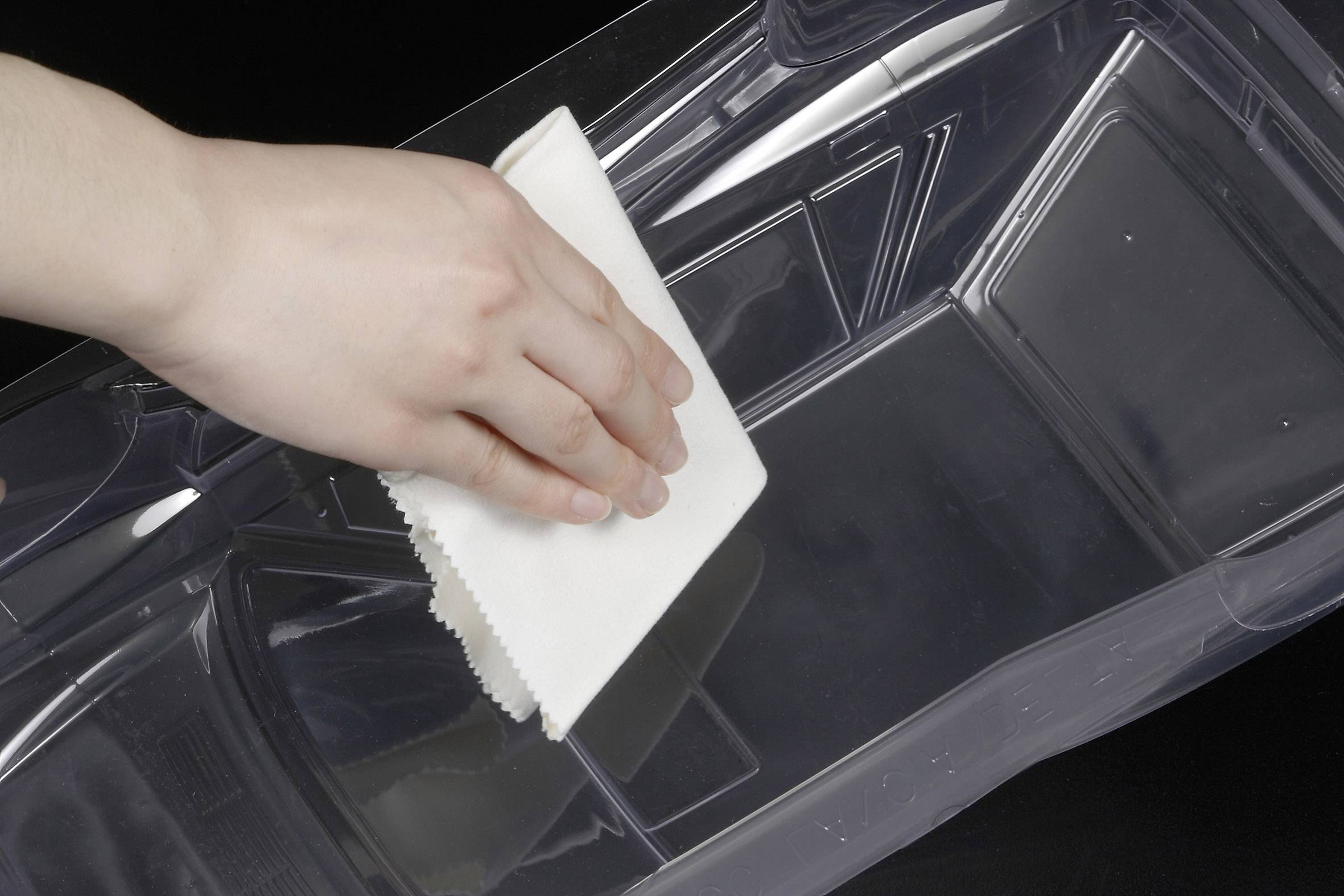 Une main essuie une surface en plastique transparente avec un chiffon blanc.