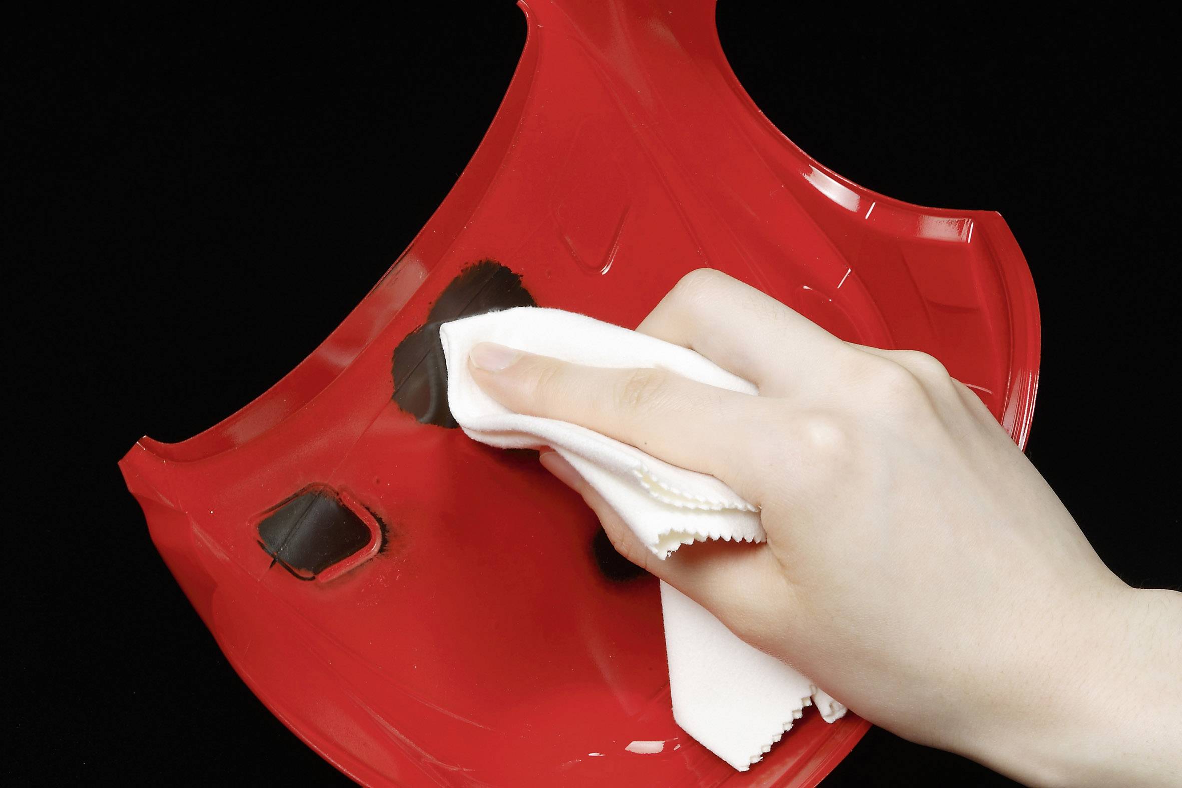 Une main nettoie un casque de moto rouge avec un chiffon blanc.