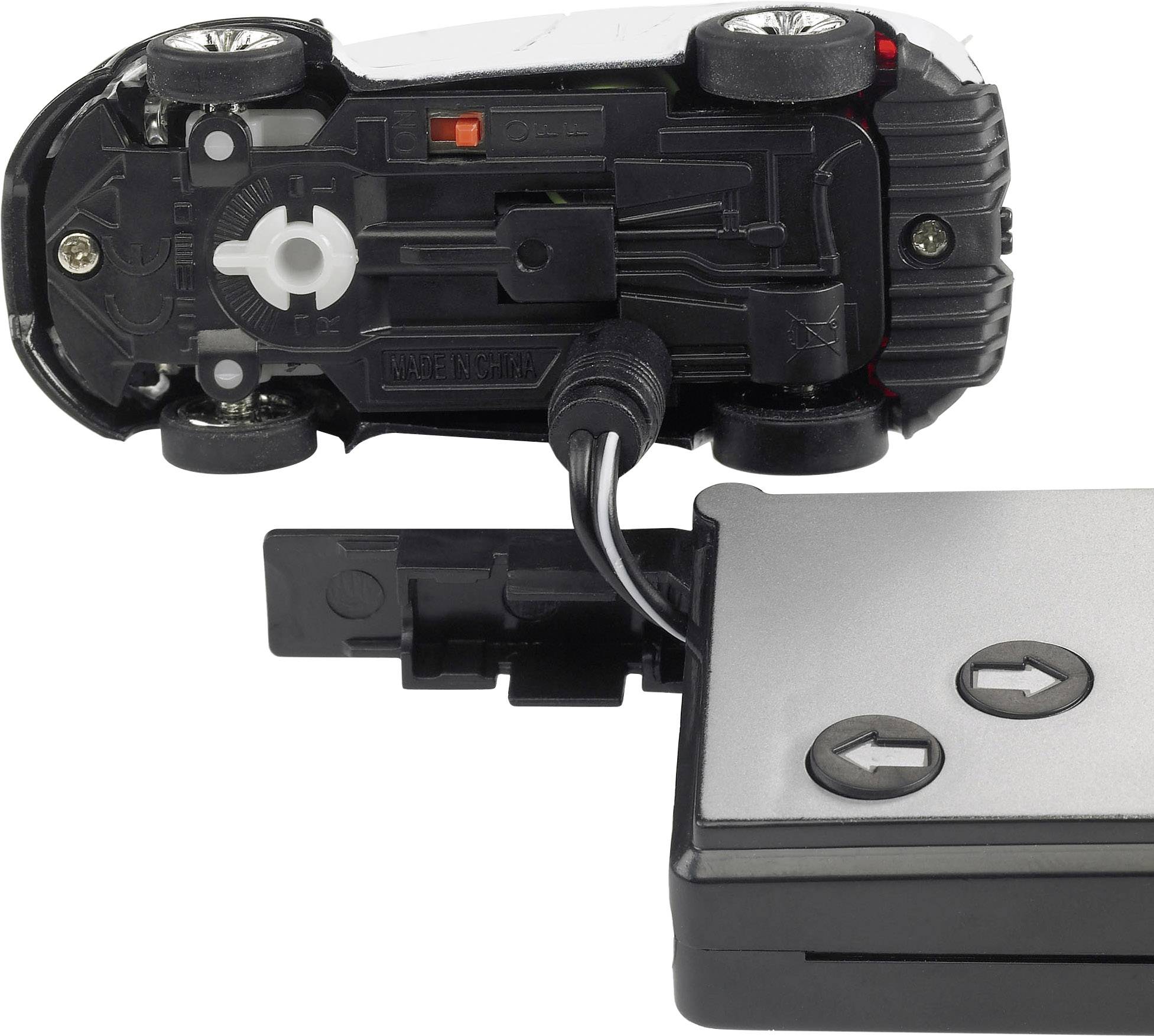 Petite voiture télécommandée avec connexion filaire pour le contrôle. La voiture est posée sur le dos, avec une télécommande munie de deux touches fléchées en dessous.