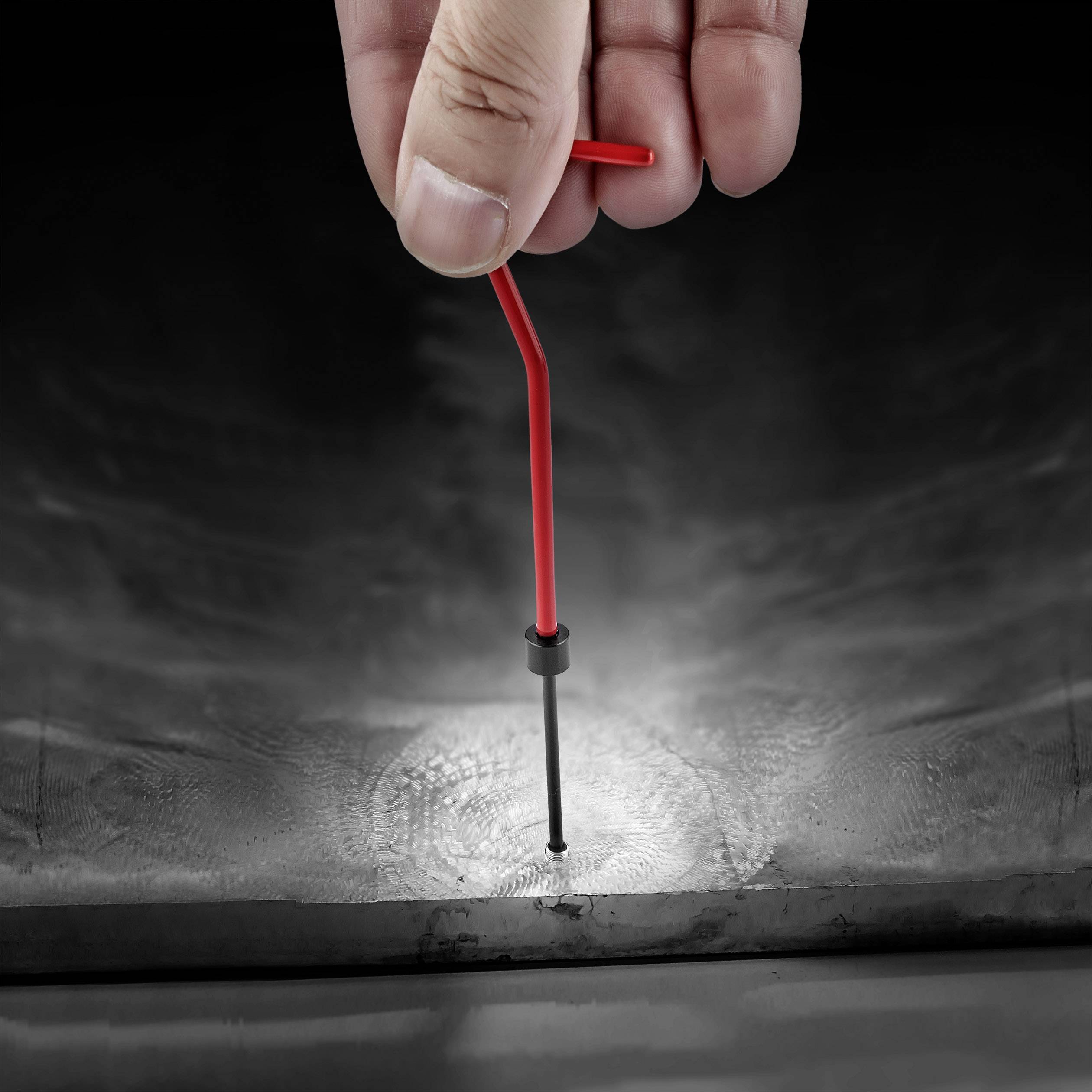 Une main retire une clé rouge d'une surface inclinée. La clé est placée dans un conduit cylindrique.