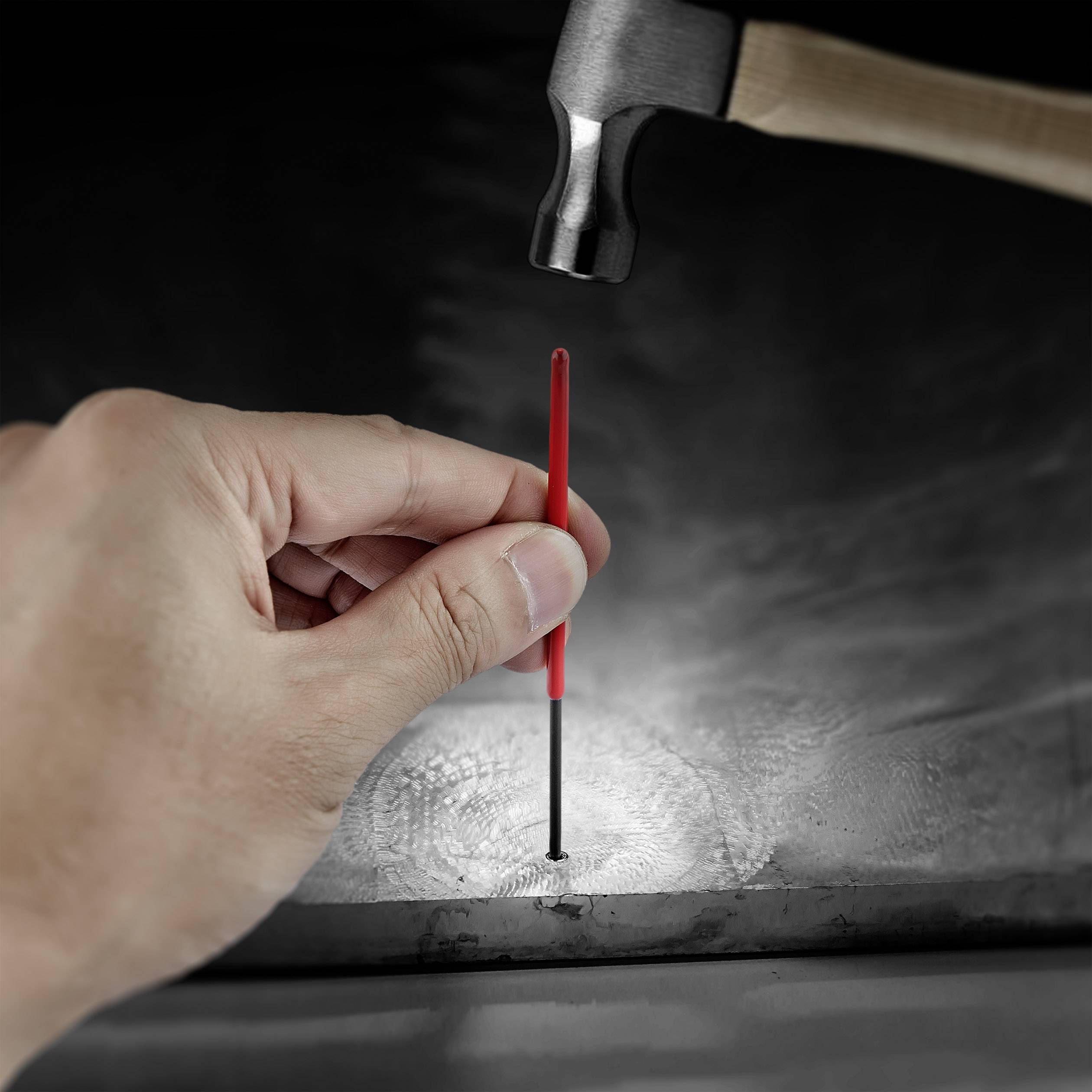 Une main tient un stylo rouge sur un clou, tandis qu'un marteau plane au-dessus du clou, prêt à le faire pénétrer.