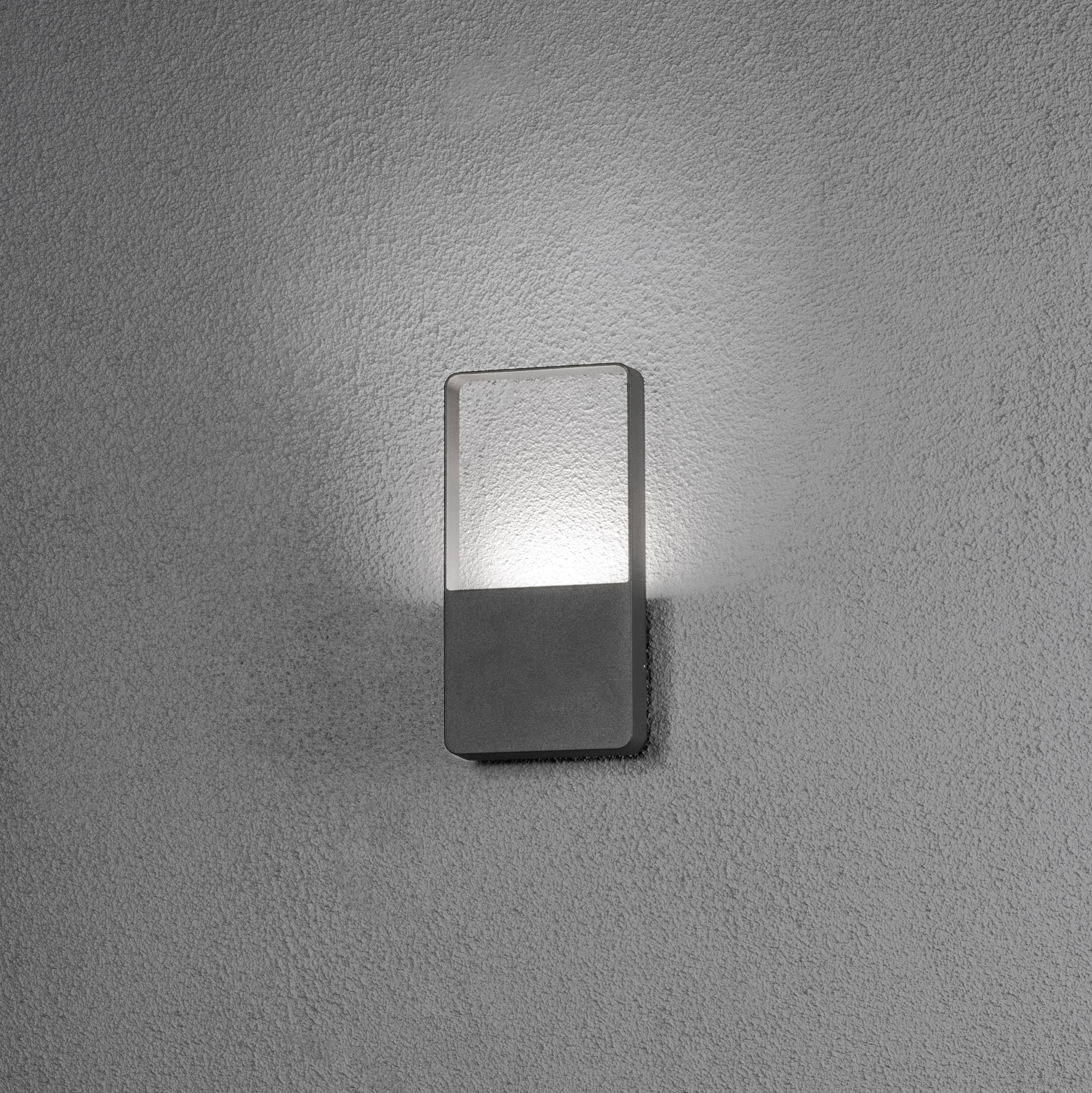 Applique murale au cadre rectangulaire, diffusant une lumière chaude sur un mur gris. Design moderne et minimaliste.