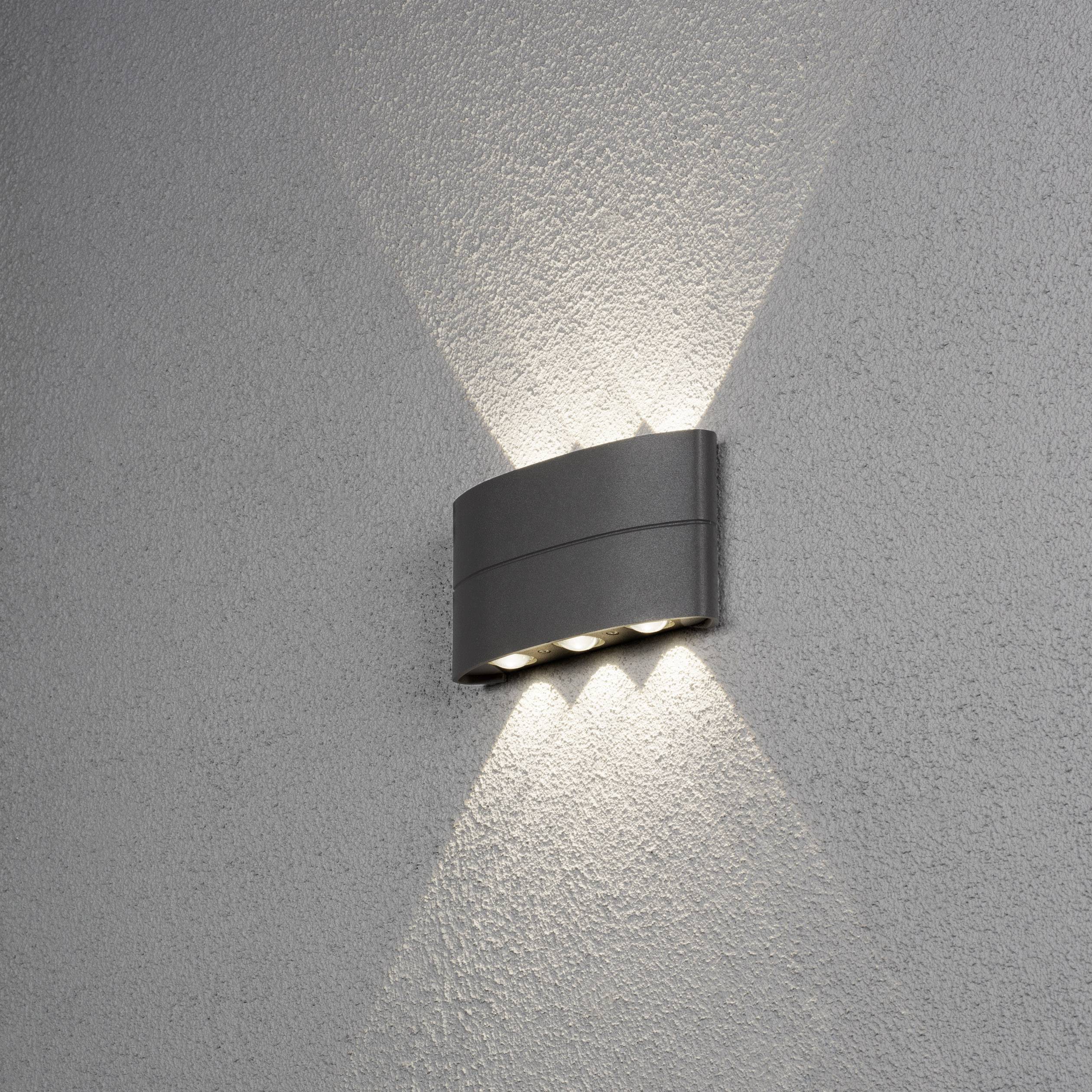 Applique murale éclairant un mur gris avec des rayons lumineux dirigés vers le haut et le bas, créant une ambiance chaleureuse et intimiste.