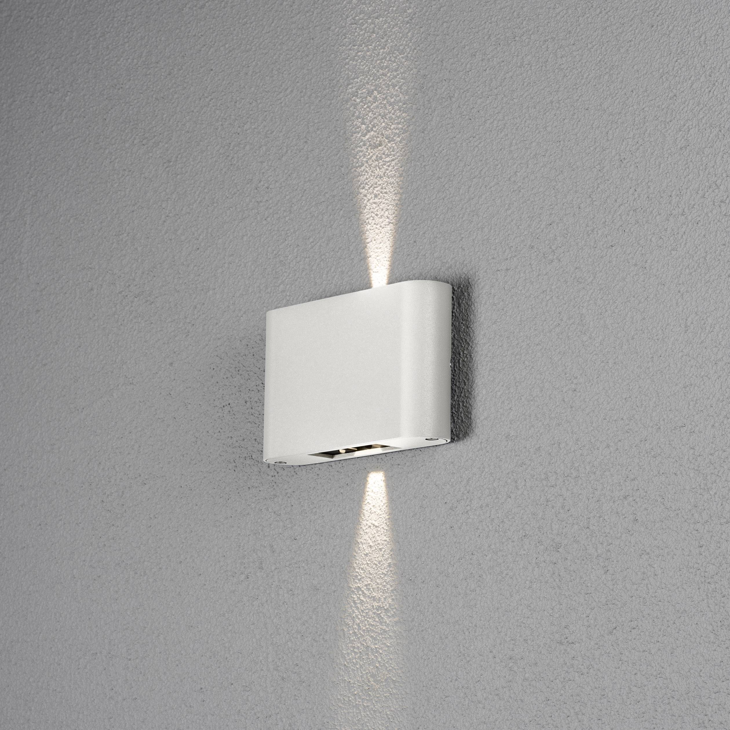 Applique murale blanche au design moderne, projetant de la lumière vers le haut et le bas sur un mur gris.