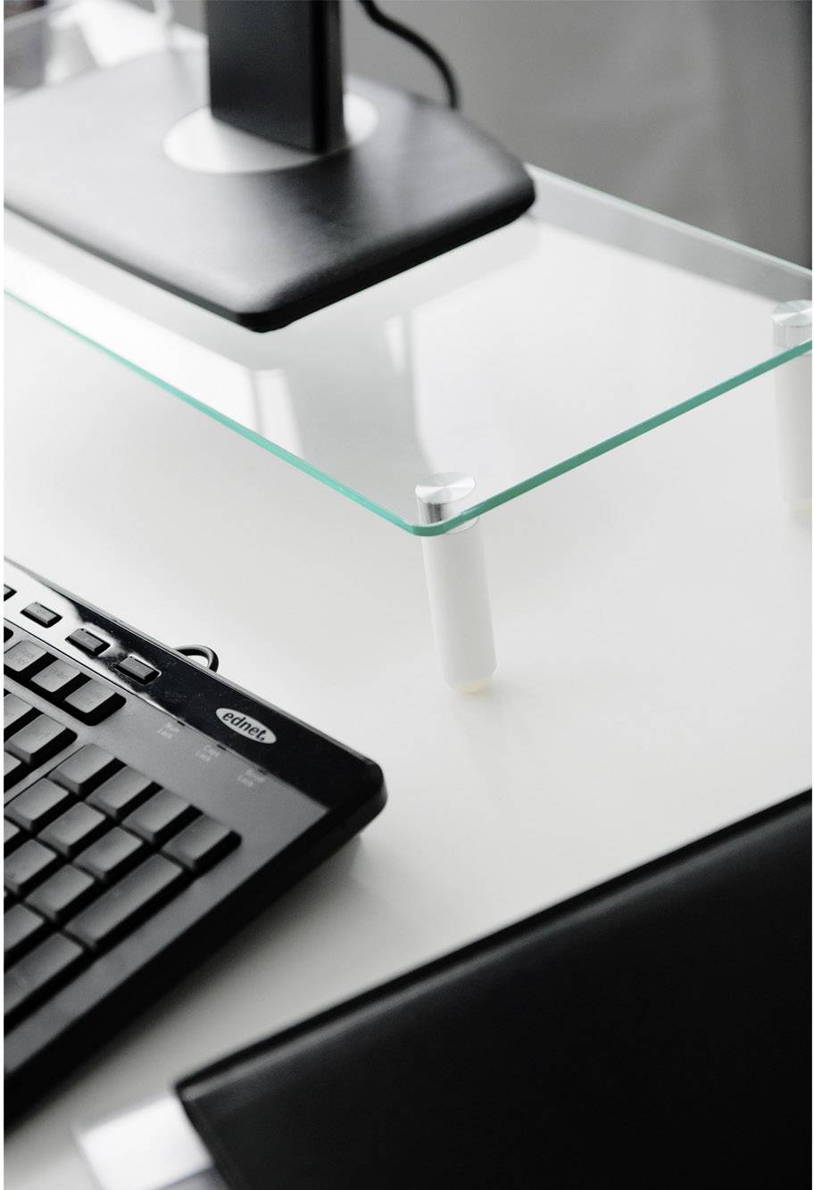 Clavier posé sur un bureau blanc avec une tablette en verre et un support de moniteur. Il traduit un environnement de travail propre et organisé.