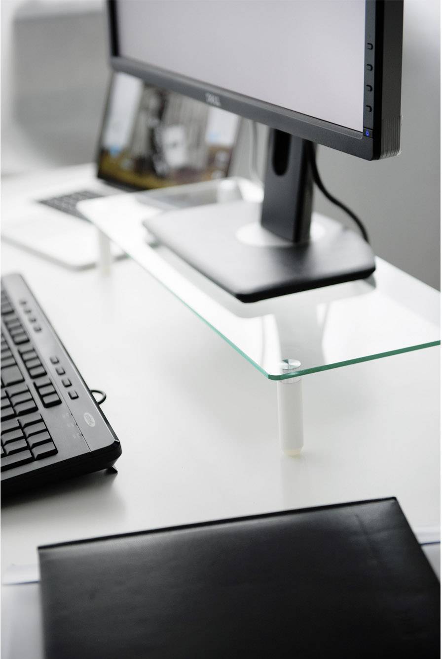 Un écran d'ordinateur est posé sur une étagère en verre sur un bureau, à côté se trouve un clavier et un ordinateur portable en arrière-plan.