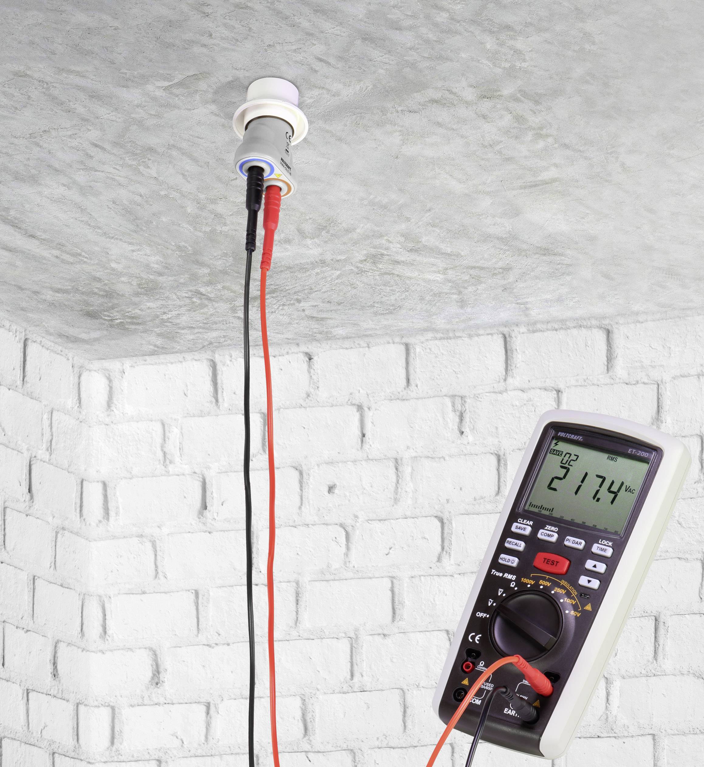 Un multimètre mesure la tension d'un plafonnier, affichant 217,4 volts sur son écran. Les câbles rouge et noir sont branchés.