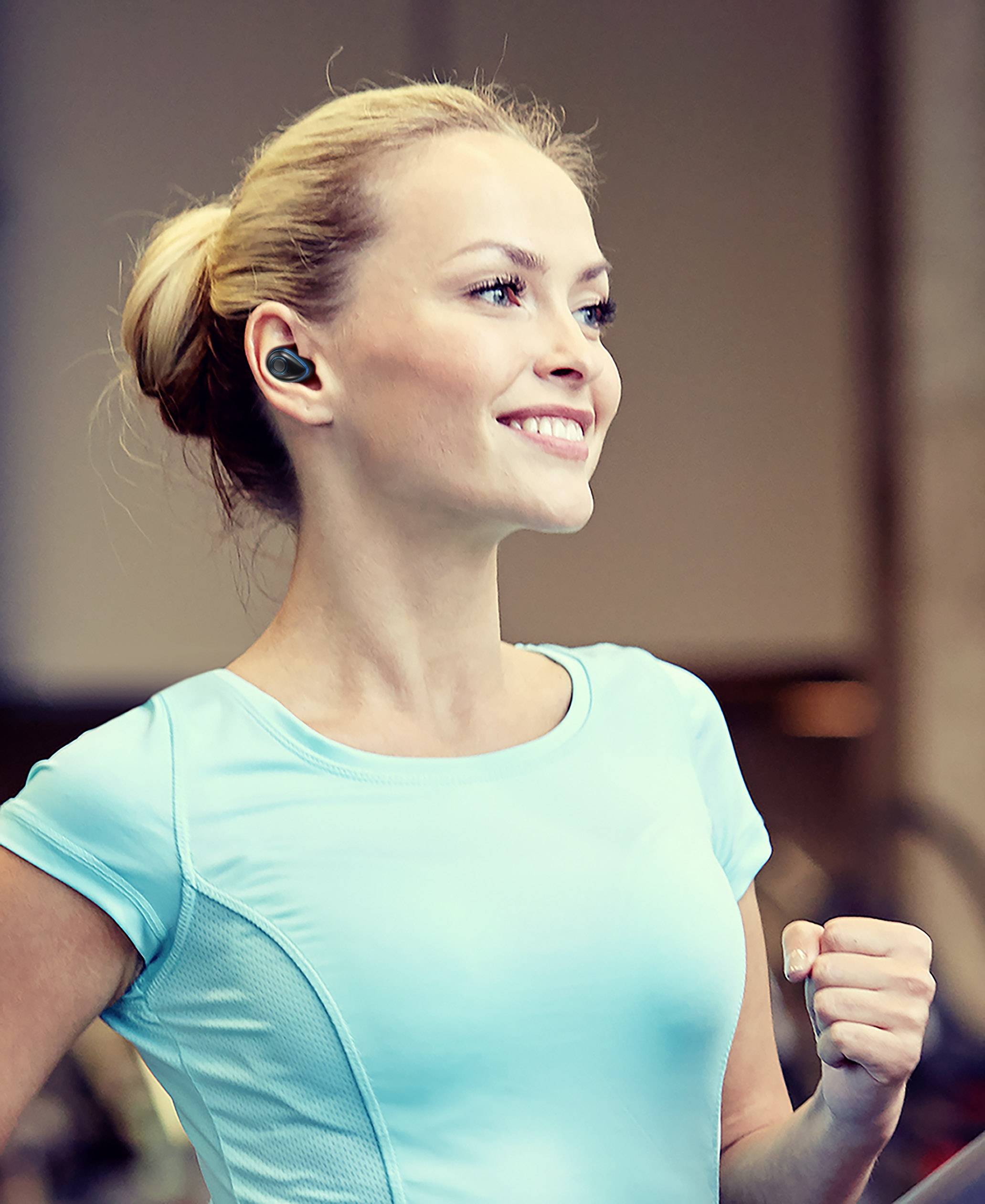 Une femme souriante en tenue de sport avec des écouteurs sans fil court à l'intérieur.